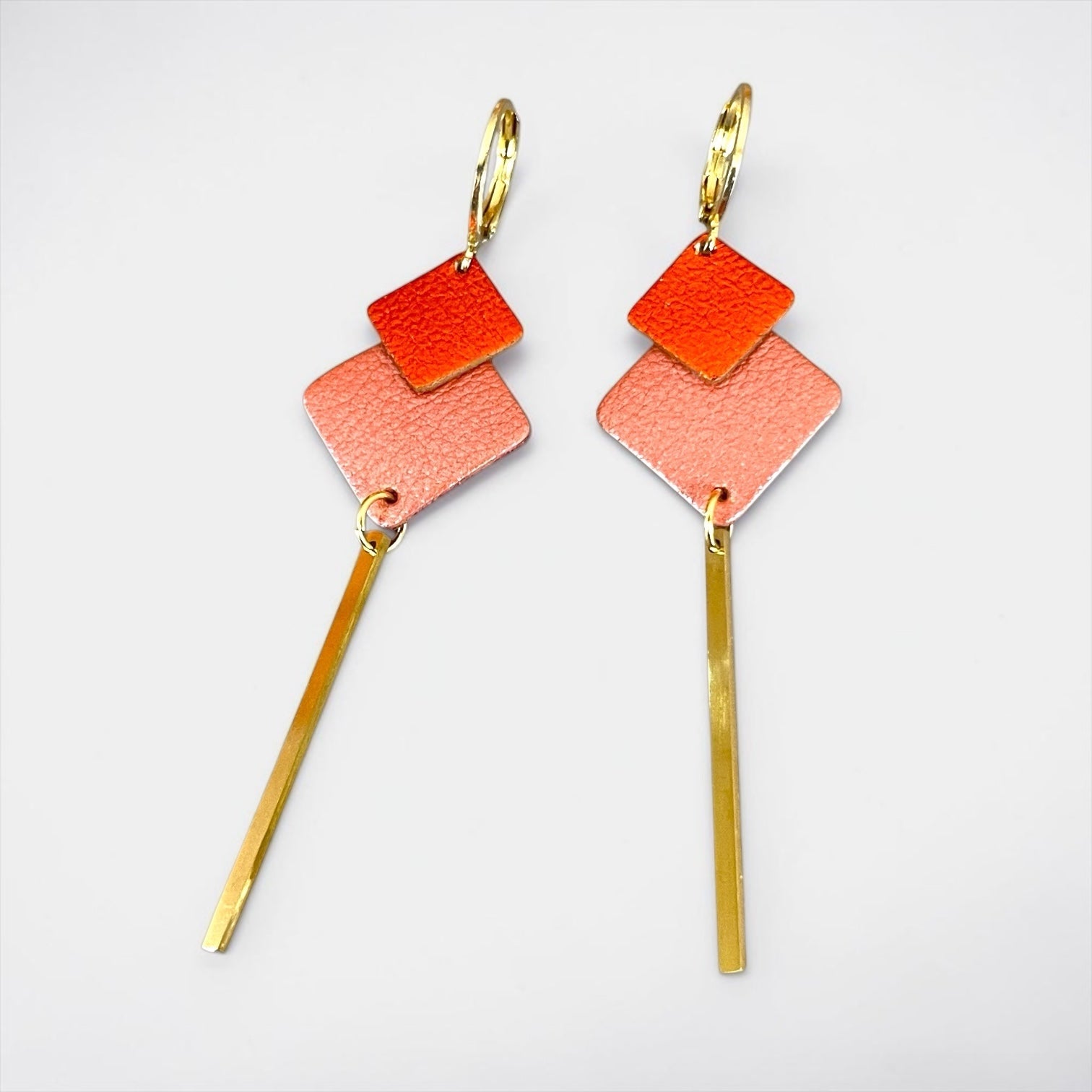 boucles d'oreilles dorées Nune modèle Ada avec duo de losanges en cuirs Corail nacré et orange sanguine métallisé terminées par longue tige fine dorée, sur fond blanc