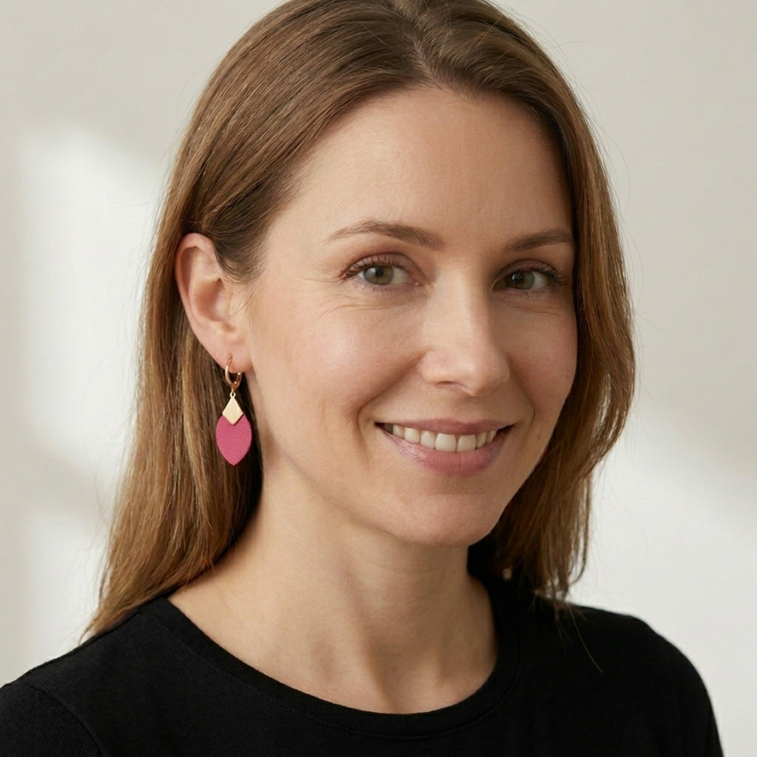 Petites boucles d'oreilles dorées en forme d'olive modèle Olivia en cuir rose fushia portées aux oreilles par une femme blonde