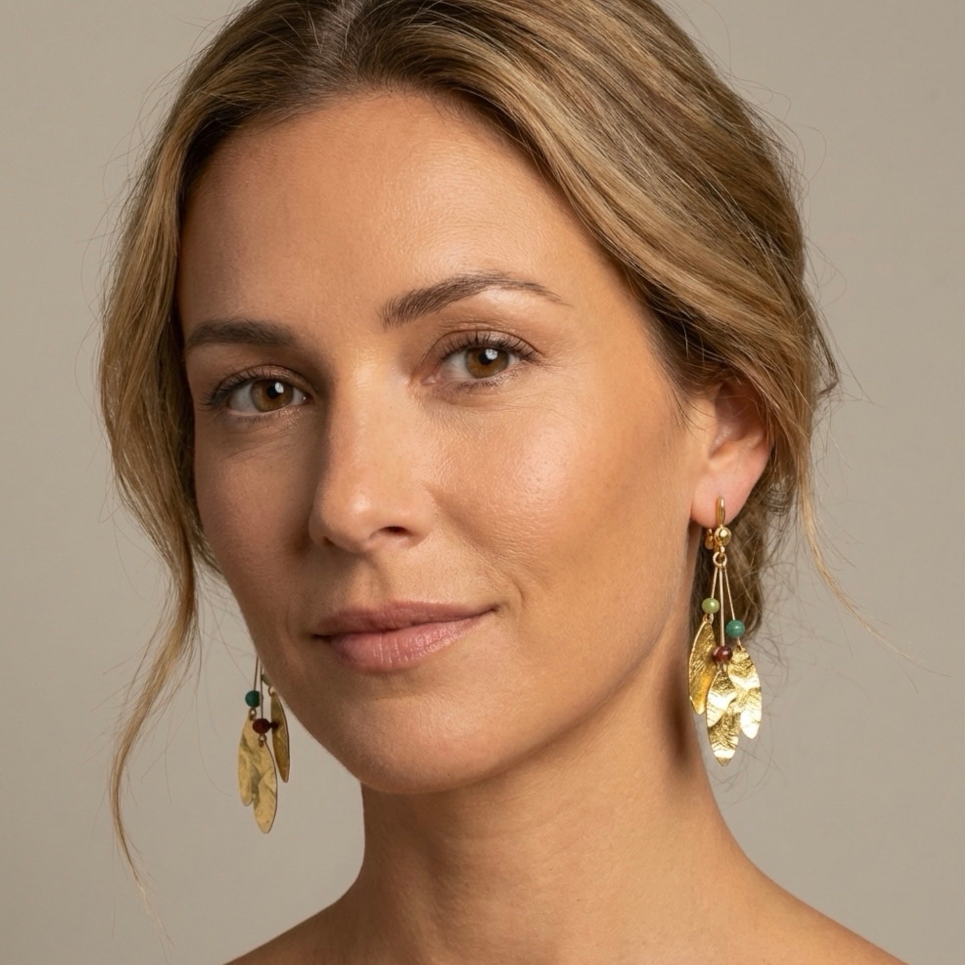 Longues boucles d'oreilles fines modele Côme de Nune avec trois pointes en métal martelé doré à l'or fin et petites perles de pierres naturelles, portées aux oreilles par une femme blonde