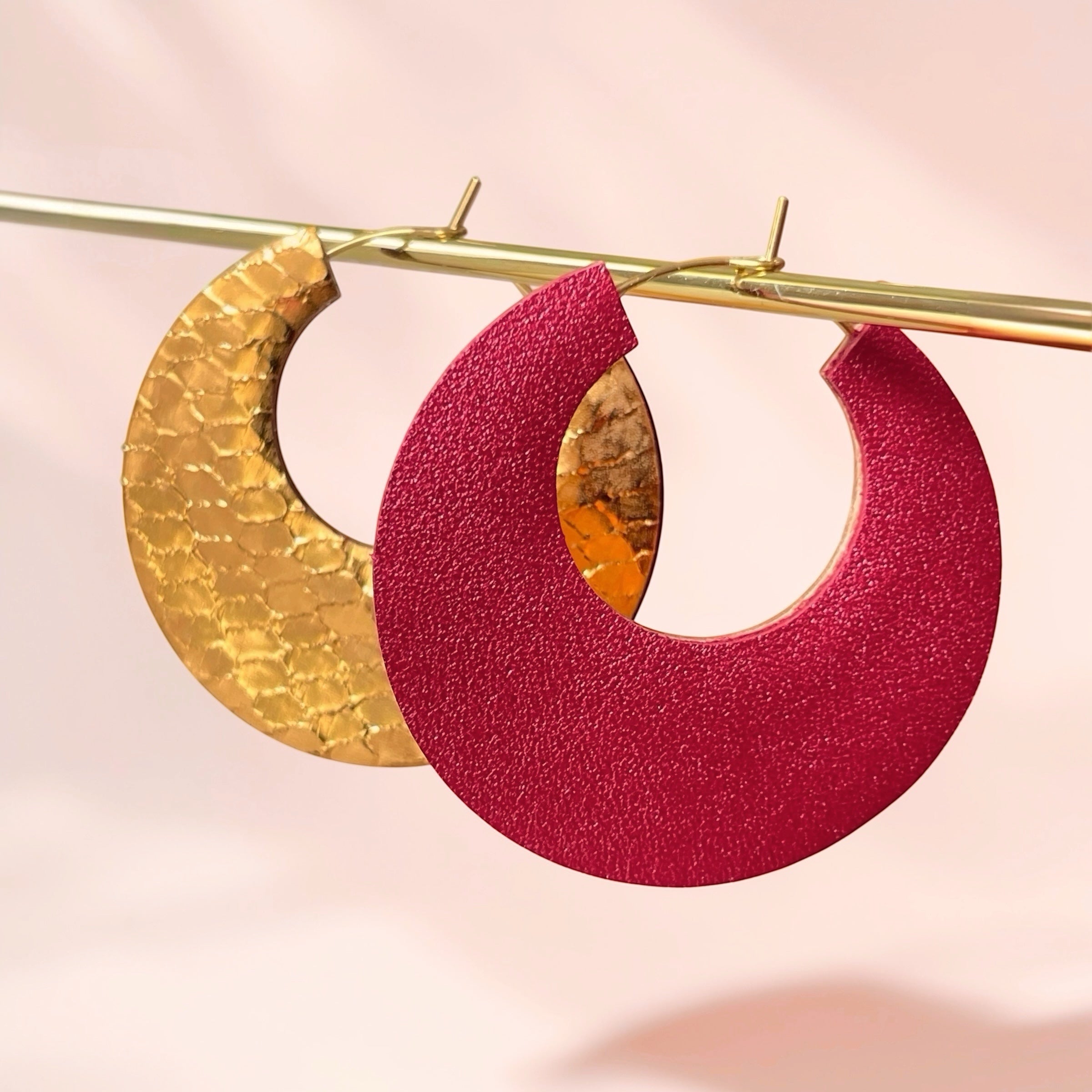 NUNE grandes boucles d'oreilles créoles dorées rondes tout-cuir Circus, un côté rubis métallisé, l'autre côté bronze brillant façon serpent, pendues sur un portant doré