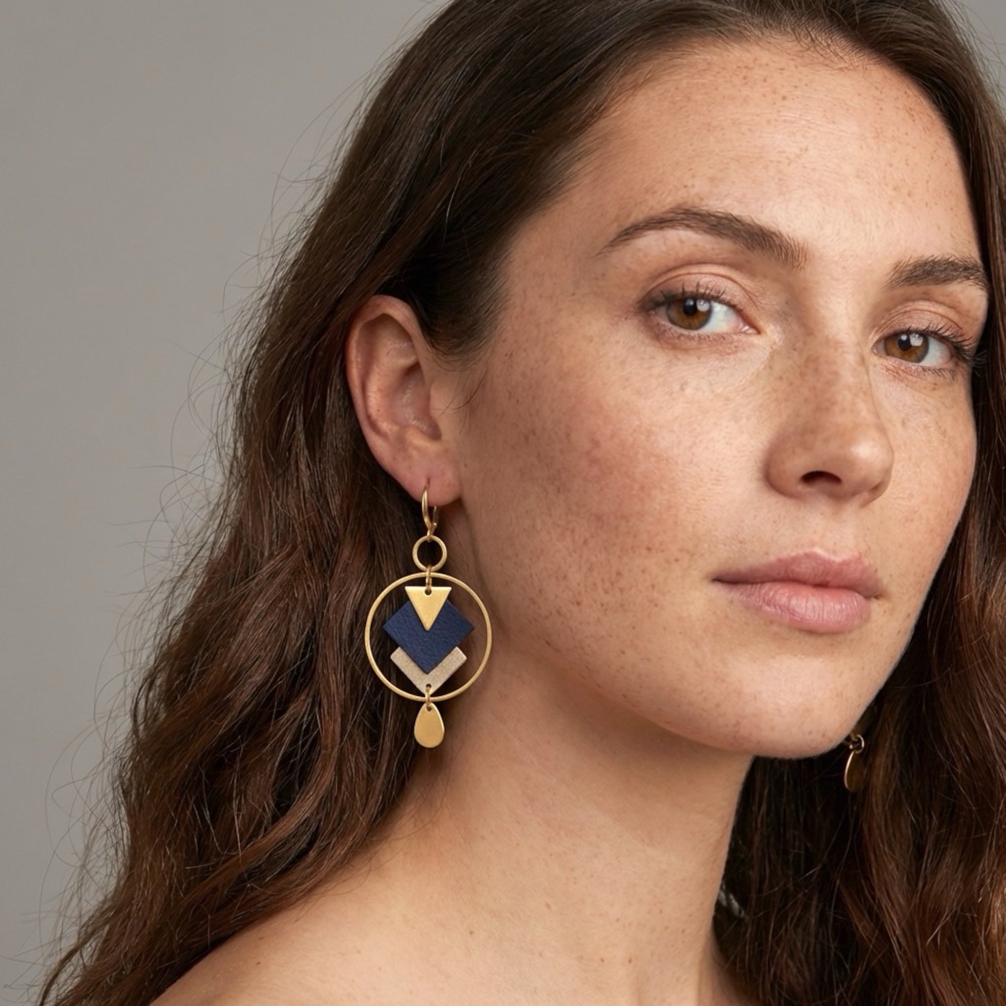Boucles d'oreilles Nune modèle Créoles Adamante Or en cuir bleu marine grainé et laiton doré à l'or fin Portées par une femme brune