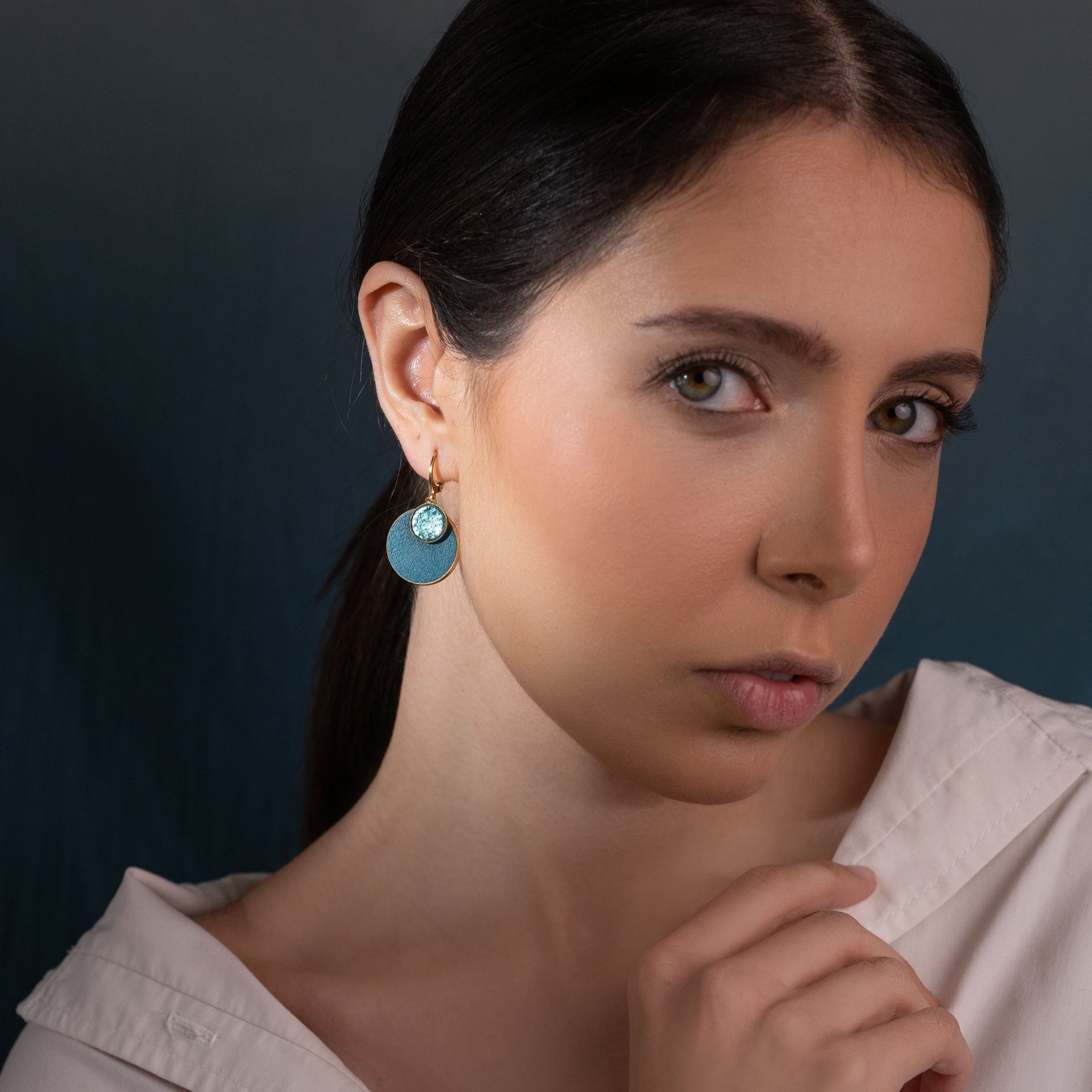 Petites boucles d'oreilles dorées rondes Nune modèle Bulles avec doubles sertis de cuirs vert émeraude brillant et vert canard, portées à l'oreille par une femme brune