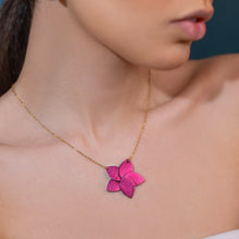 Charger l'image dans la galerie, Collier doré court avec pendentif en cuir fushia métallisé en forme de fleur, porté par une femme brune