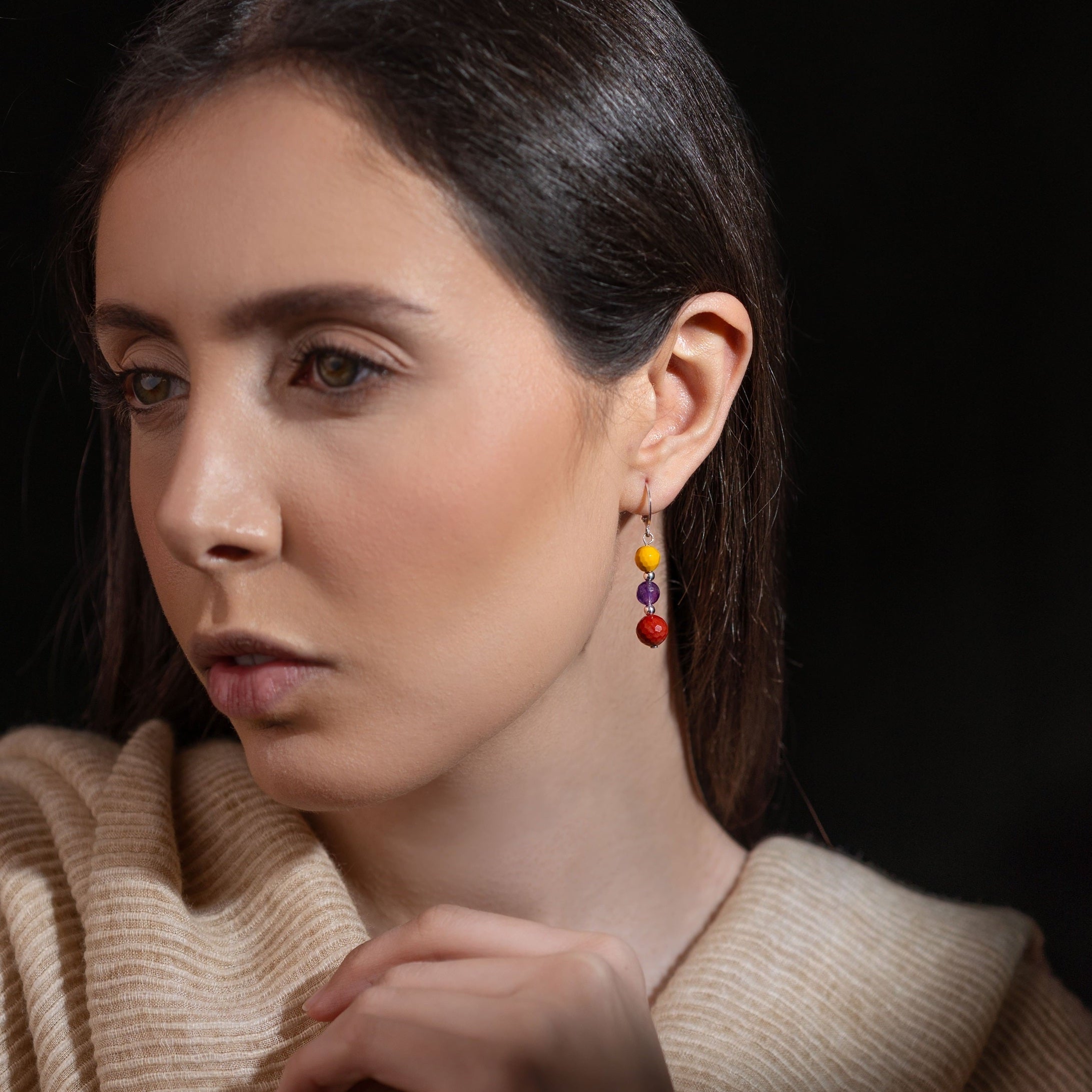 Boucles d'oreilles pendantes argentées en perles de pierres naturelles colorées, portées à l'oreille par une femme brune