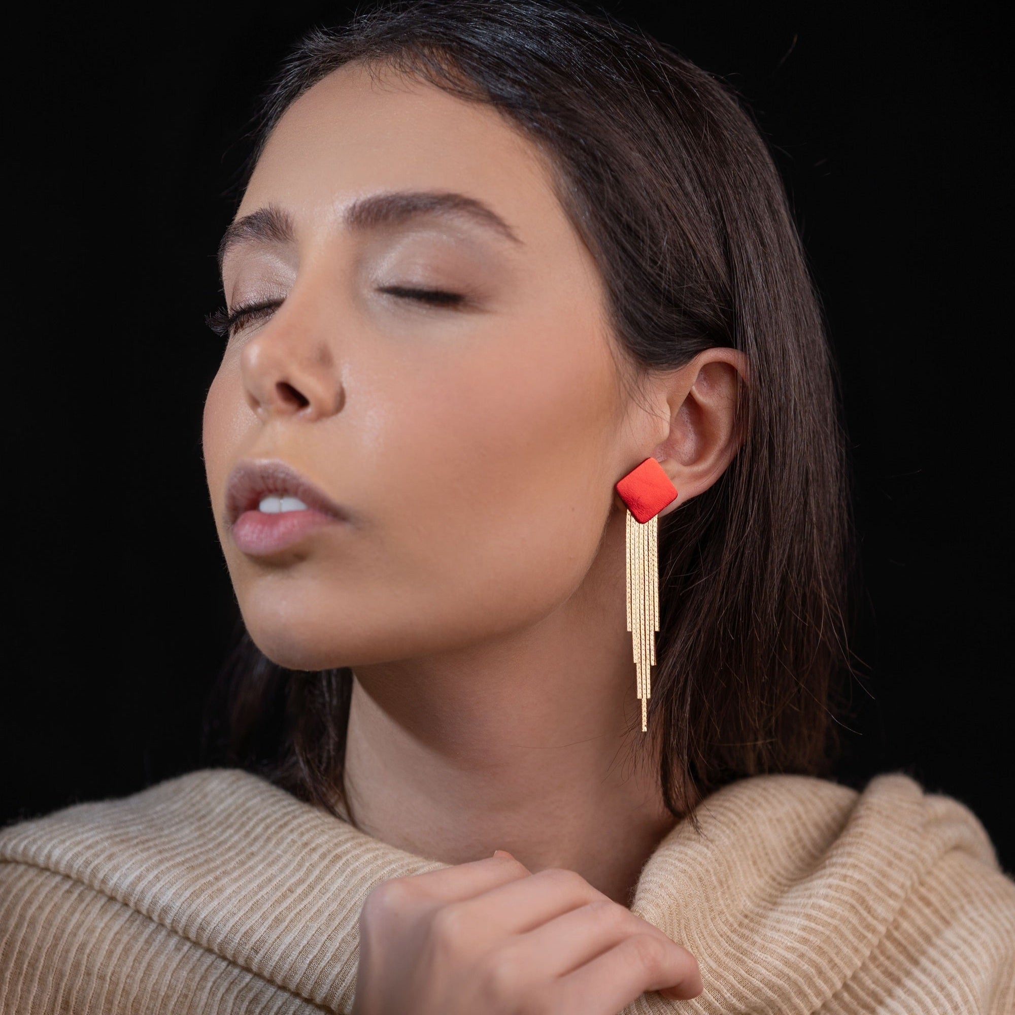 Puces d'oreilles losanges en cuir rouge métallisé avec leurs cascades de fines chaînettes dorées, portées à l'oreille par une femme brune