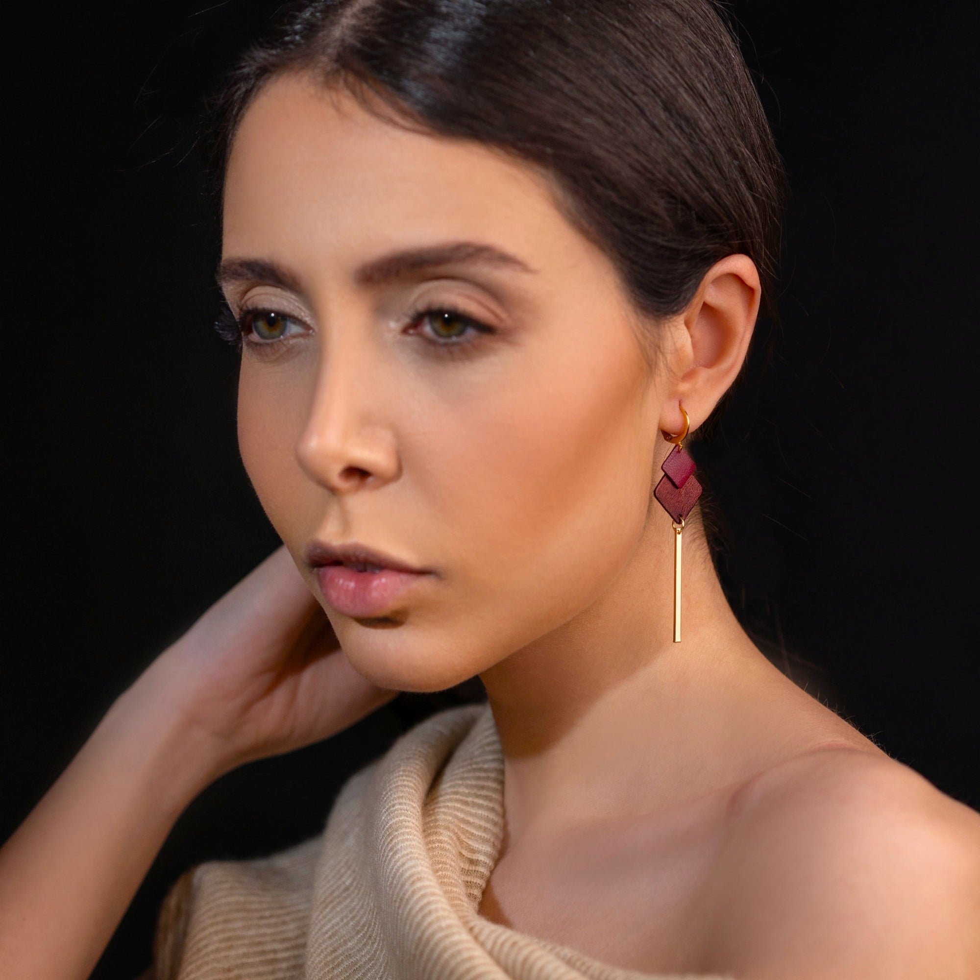 boucle d'oreille dorée Nune modèle Ada en cuirs pourpre et grenat métallisé portée par une femme brune