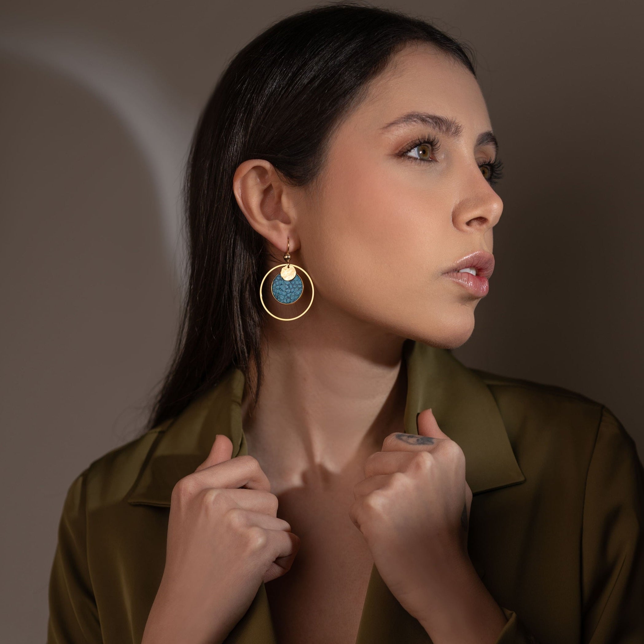 Boucles d'oreilles dorées rondes pendantes de style créoles avec sequin en cuir marin bleu paon métallisé, portées à l'oreille par une femme brune