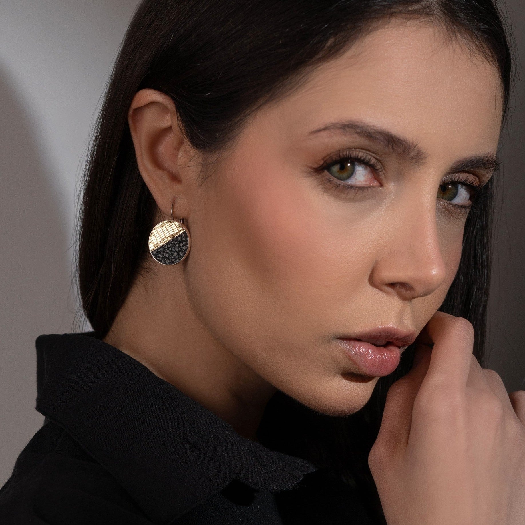 Boucles d'oreilles rondes argentées bicolores en cuirs doré façon serpent et noir grainé, portées à l'oreille par une femme brune