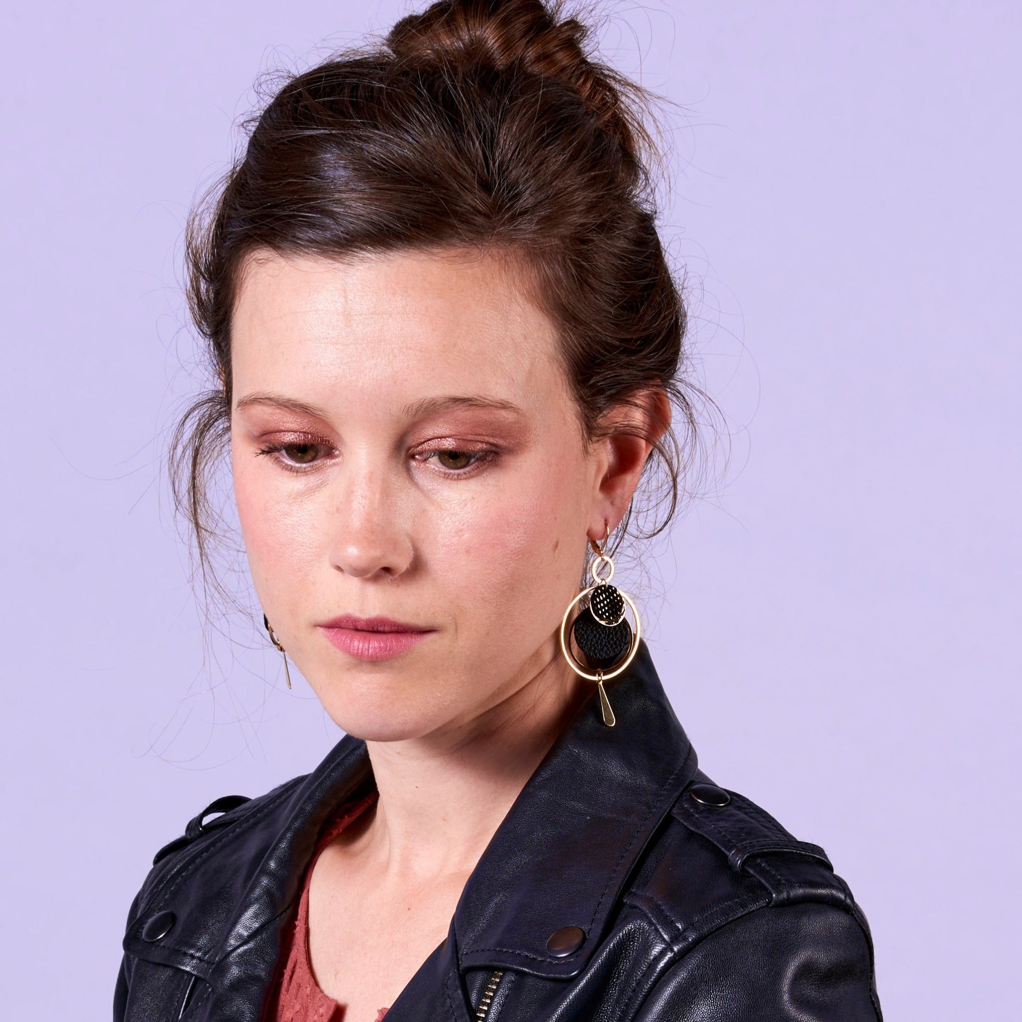 Jeune femme à chignon et perfetto portant les Boucles d'oreilles dorées Nune modèle Galassia en cuirs noir grainé et noir grainé irisé