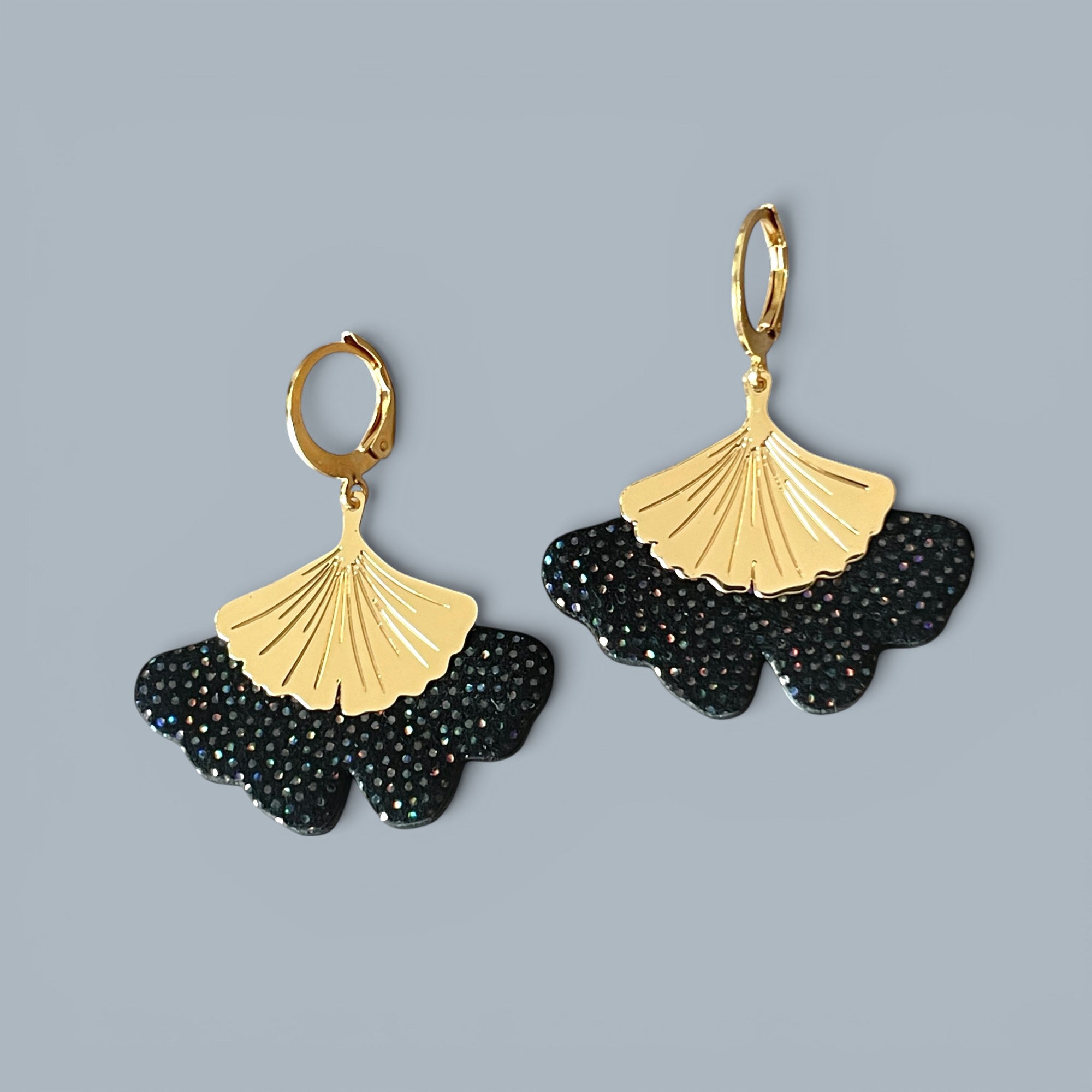 Boucles d'oreilles dorées pendantes en cuir noir à pois holographiques en forme de gingko, sur fond gris