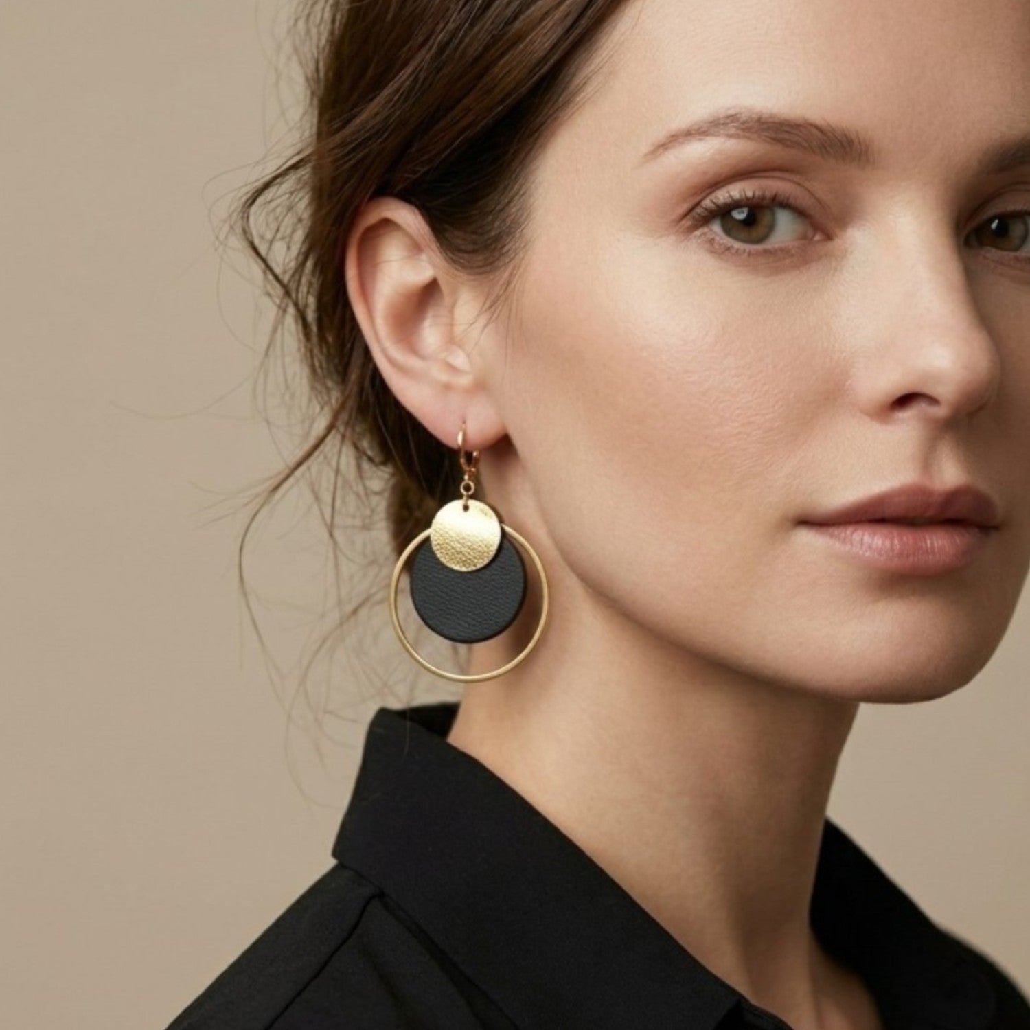 Boucles d'oreilles rondes Héra Nune en disques de cuirs upcyclés noir satiné et doré satiné avec grand anneau doré autour, portées aux oreilles