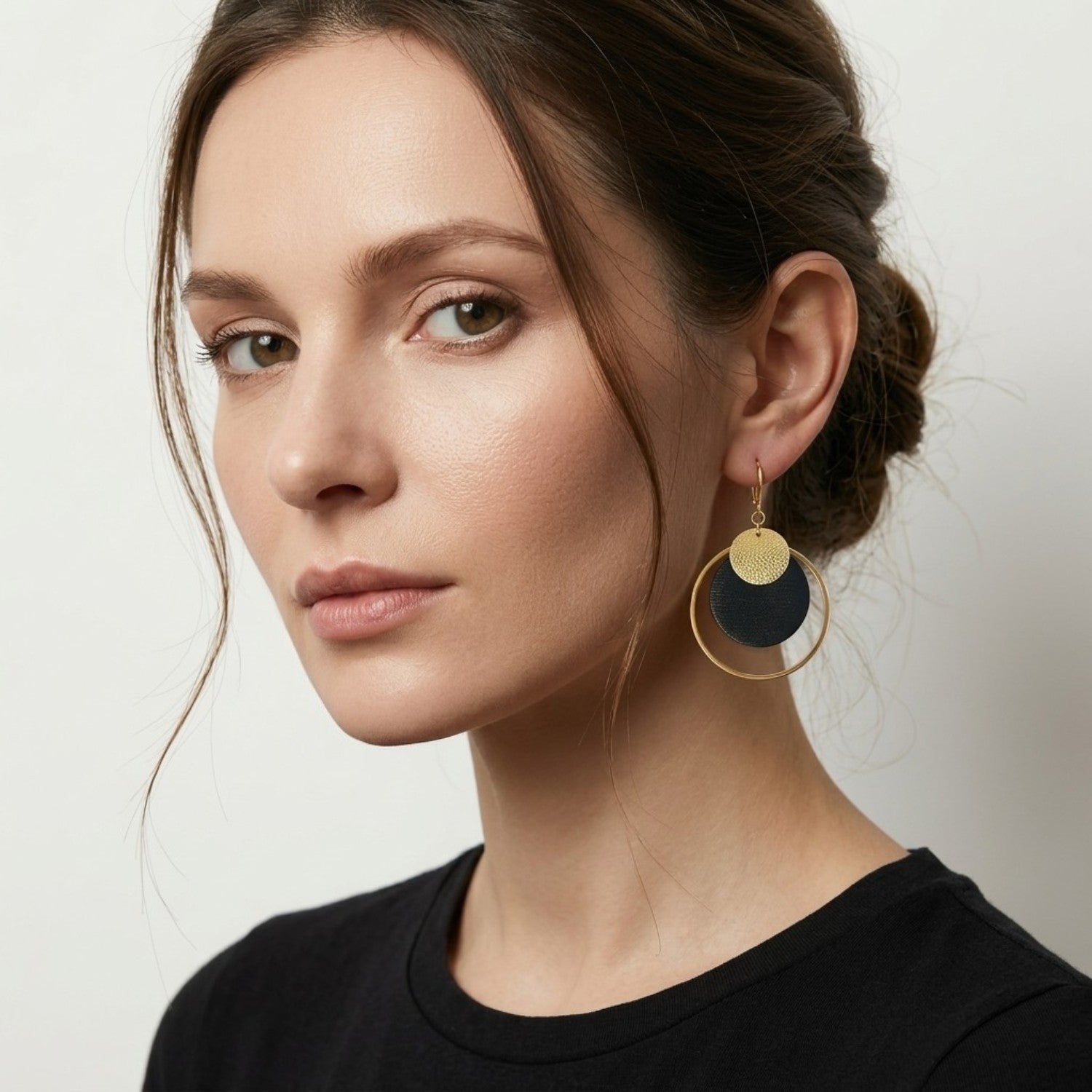 Boucles d'oreilles rondes Héra Nune en disques de cuirs upcyclés noir satiné et doré satiné avec grand anneau doré autour, portées