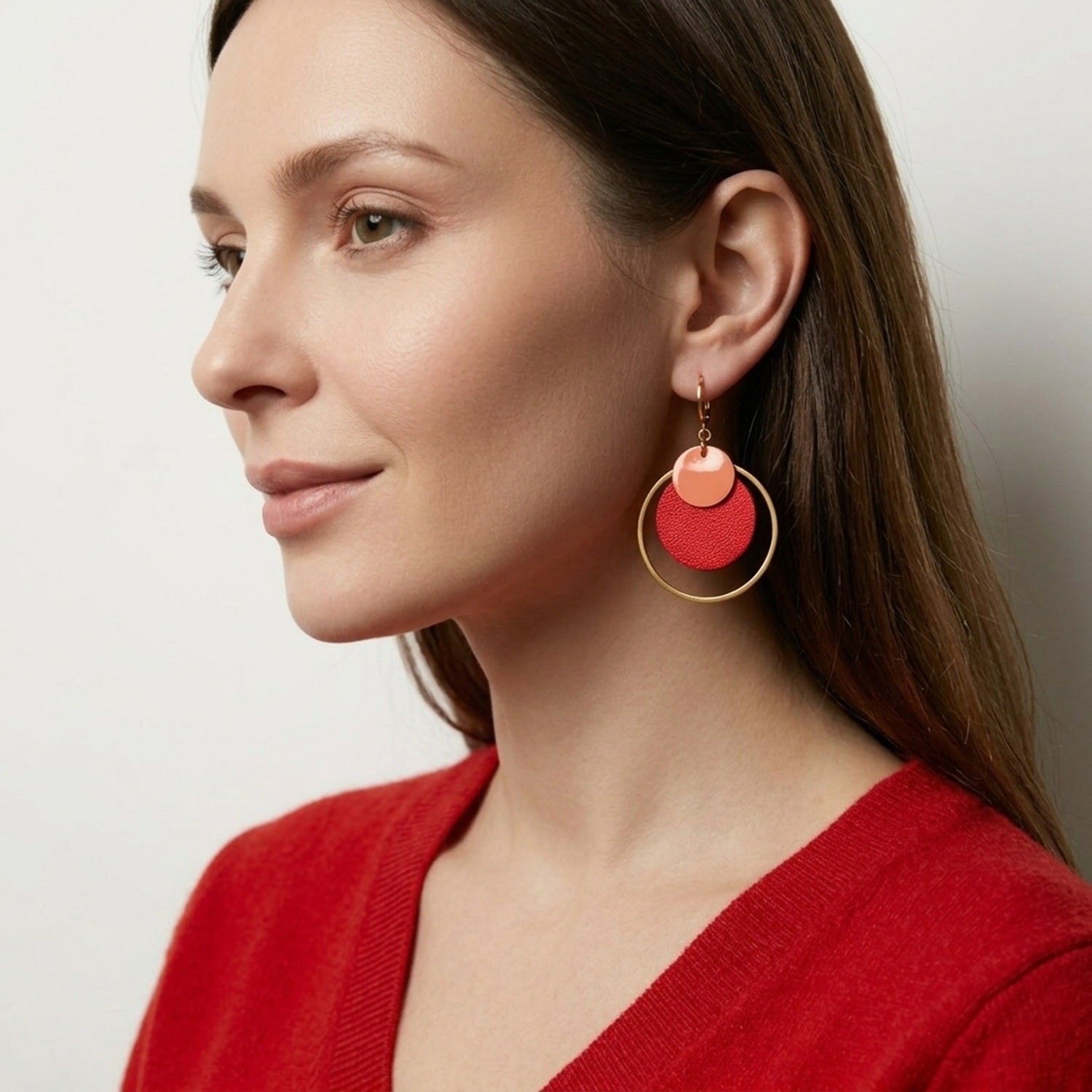 Boucles d'oreilles rondes Héra Nune en disques de cuirs upcyclés rose vernis et rouge métallisé avec grand anneau doré autour, portées aux oreilles