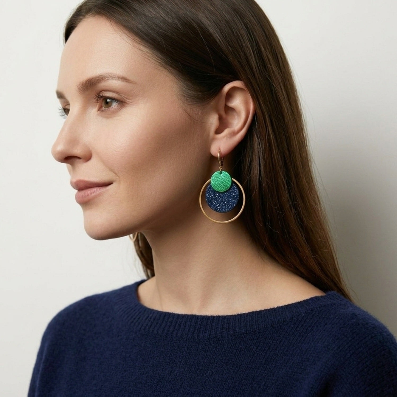 Boucles d'oreilles rondes Héra Nune en disques de cuirs upcyclés bleu marine pailleté et vert métallisé avec grand anneau doré autour, portées aux oreilles