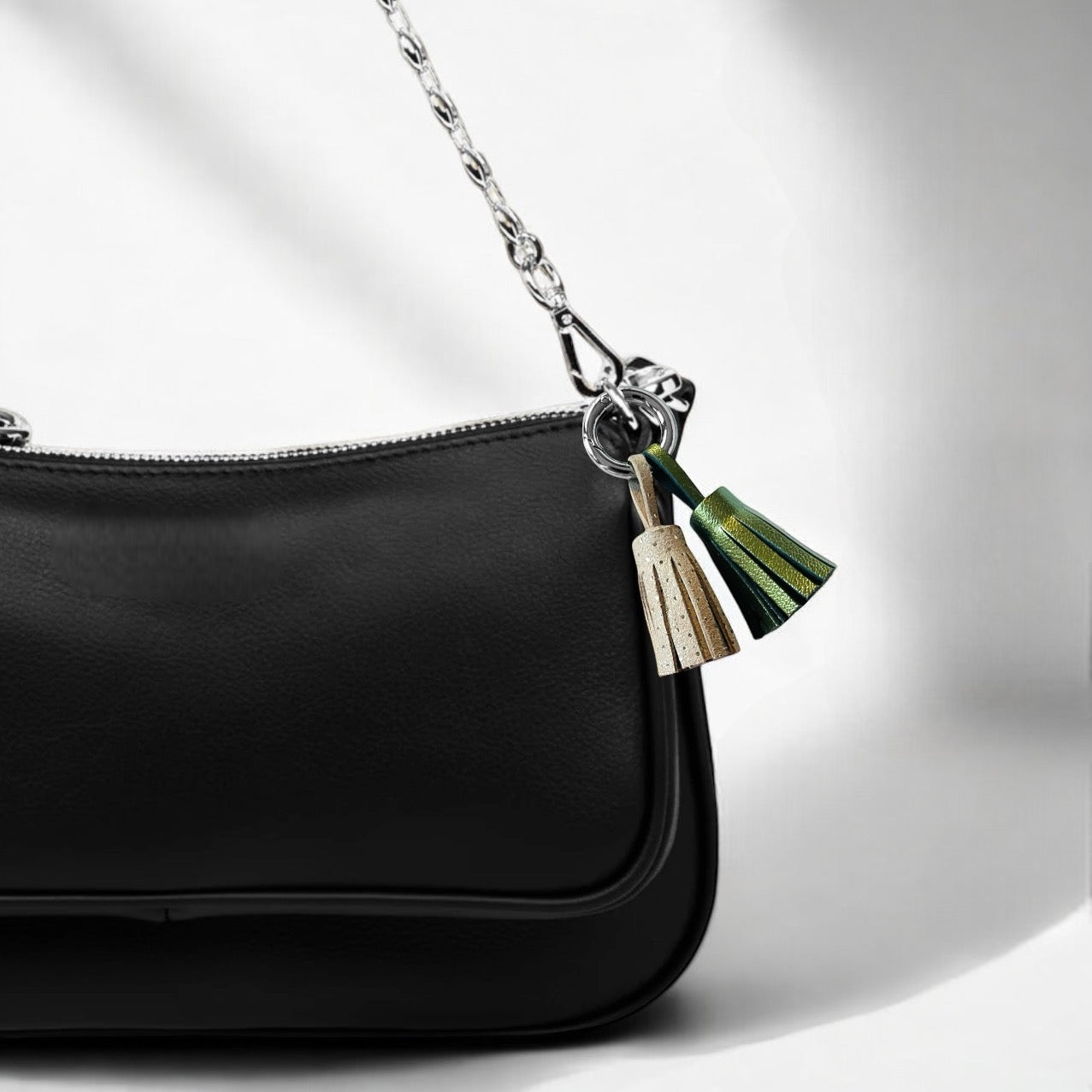 Bijou de sac argenté avec 2 pompons en cuirs beige à pois argent et kaki métallisé, accroché sur un sac à main noir