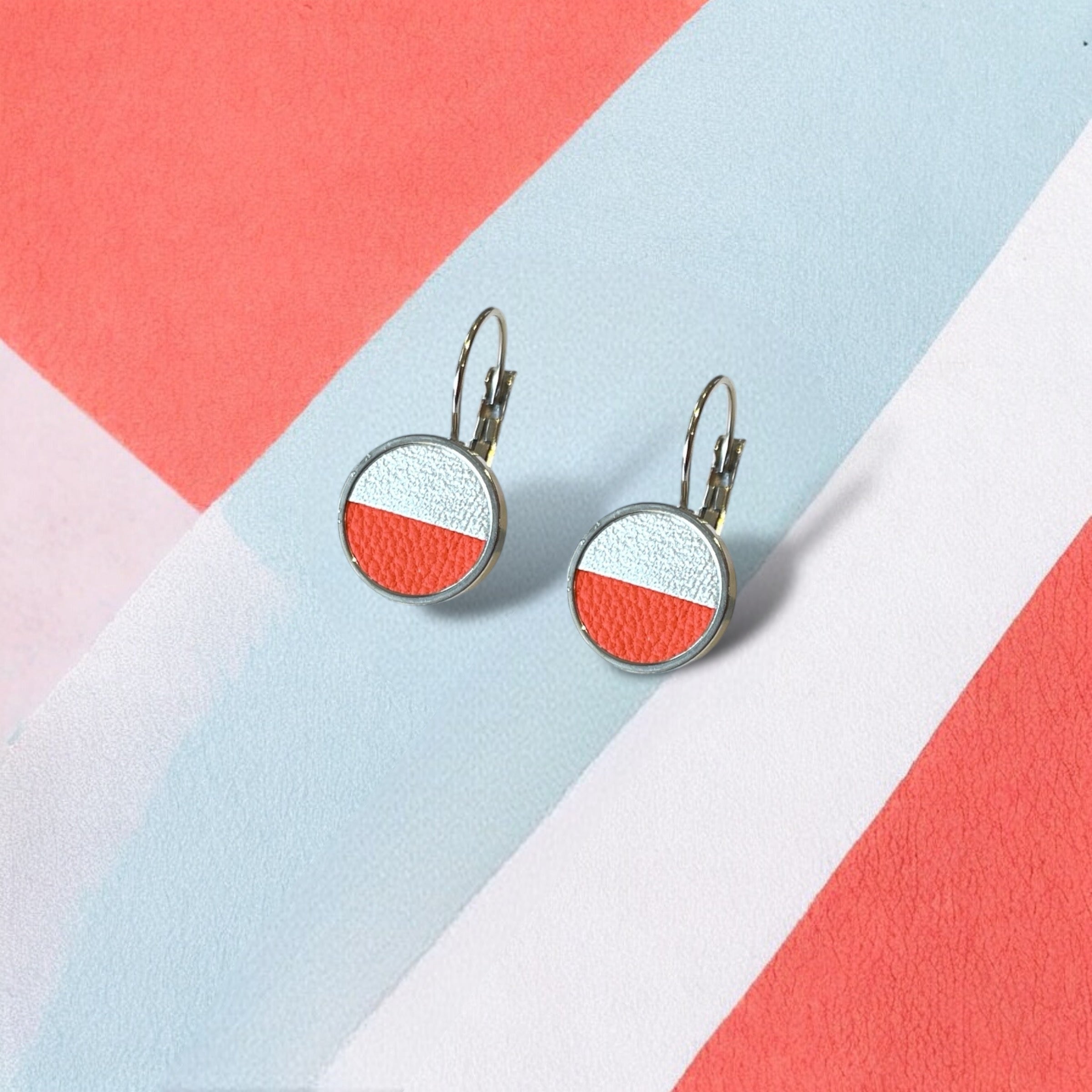 Petites boucles d'oreilles argentées pendantes rondes avec un duo de cuirs champagne nacré et carotte en cabochon, sur fond colorblock bleu pastel, orange et blanc