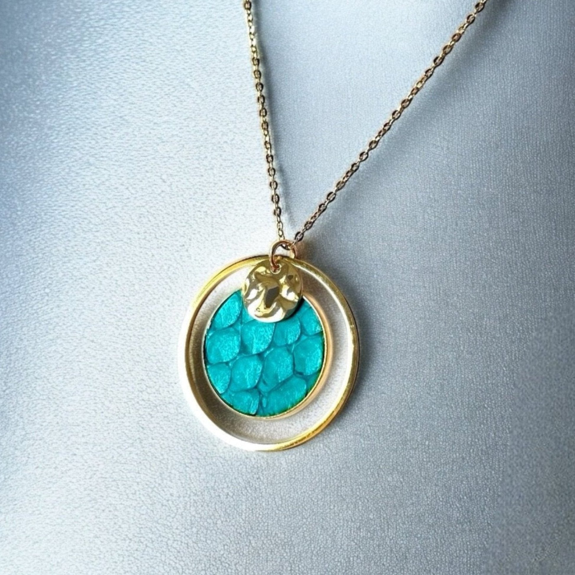 Fin collier doré avec pendentif rond en anneau avec une pièce de cuir marin bleu turquoise brut, sur fond argenté