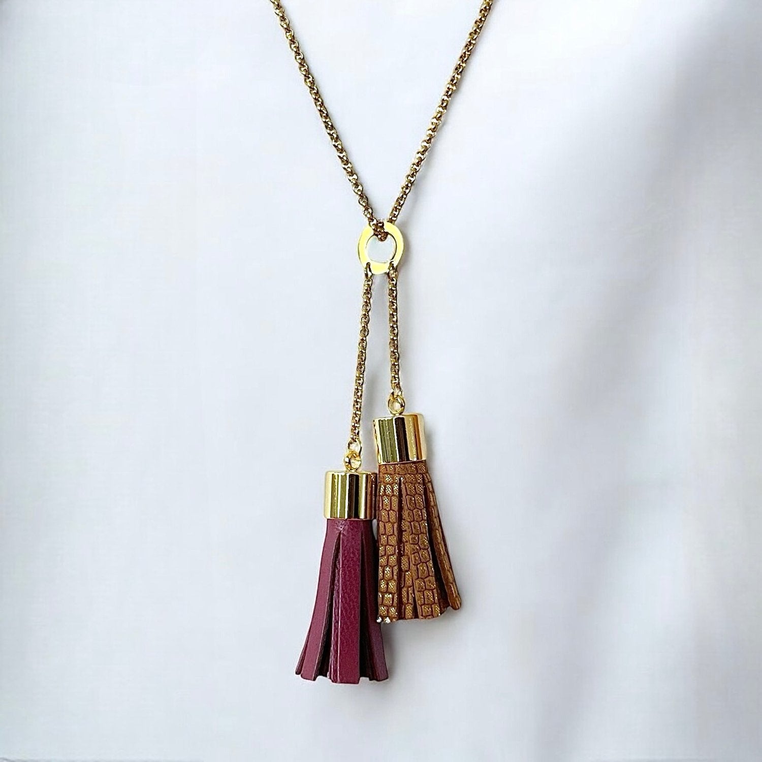 Fin sautoir doré avec pendentif en duo de pompons en cuirs pourpre et fauve or façon serpent, sur fond blanc