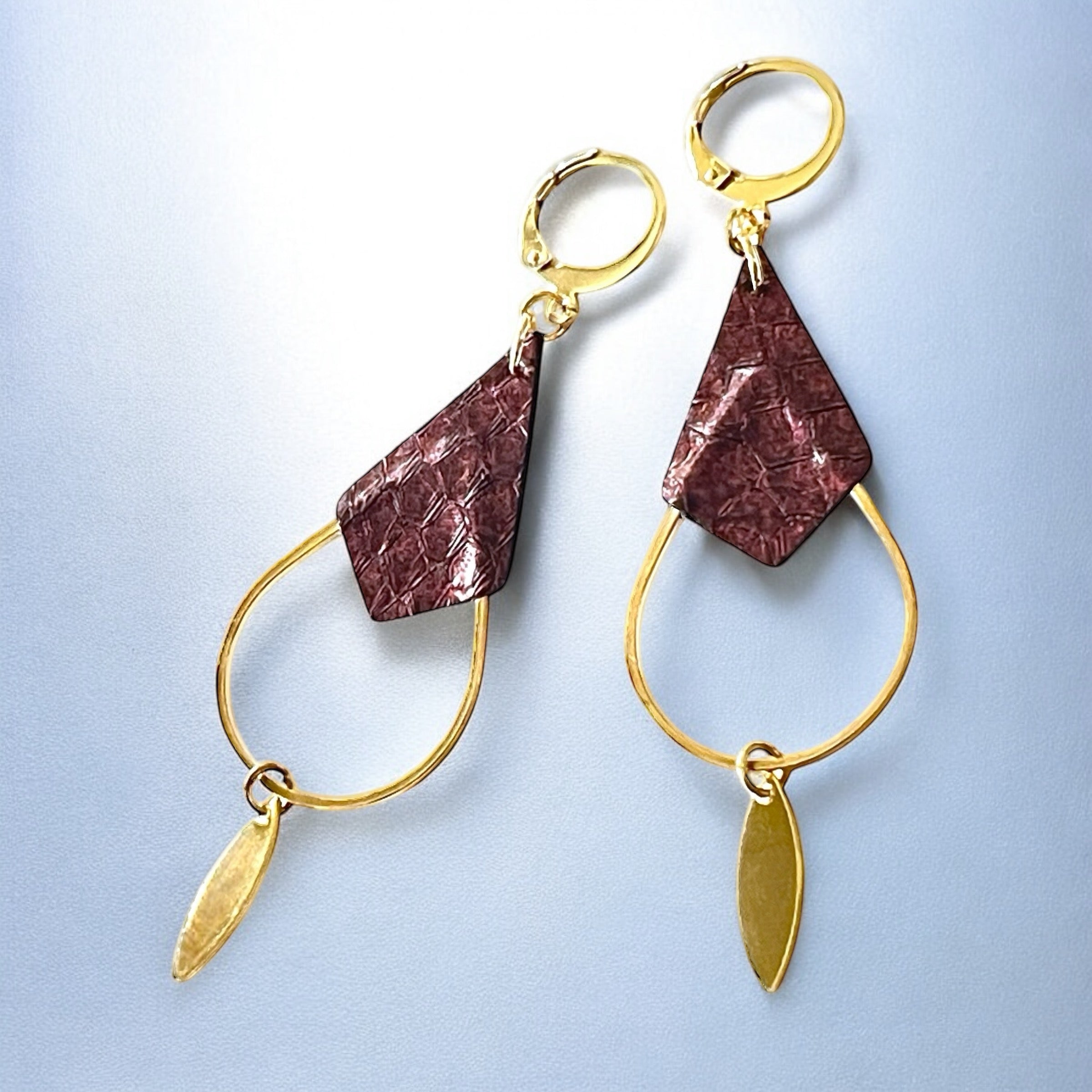 Boucles d'oreilles Gali de Nune, dorées à l'or fin avec triangle de cuir marin, cuir de poisson saumon grenat métallisé, de forme grande goutte, sur fond cuir gris