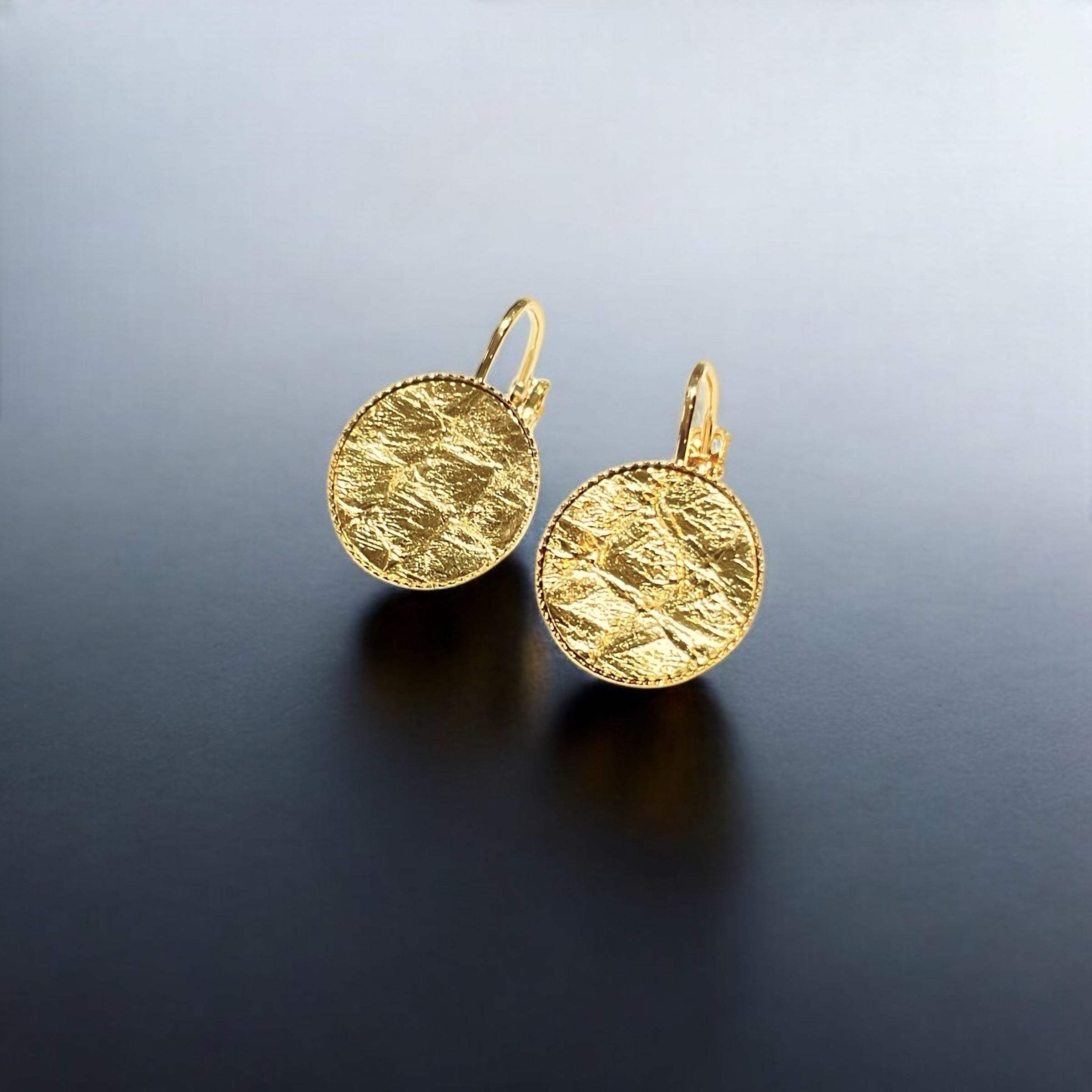 Petites boucles d'oreilles dormeuses dorées serties de fin cuir marin doré brillant, sur fond noir