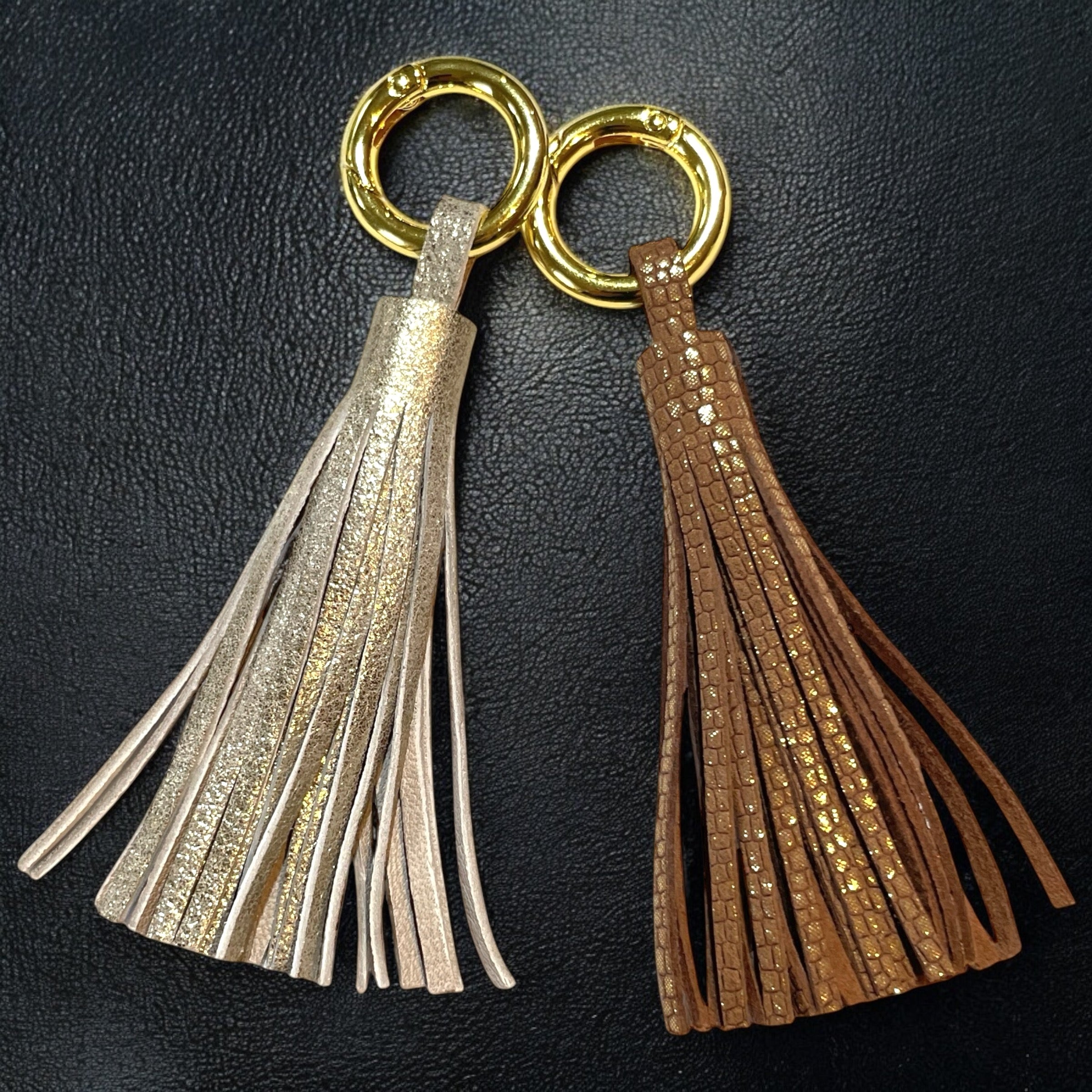 2 Bijoux de sac dorés, chacun portant un grand pompon en cuirs doré vintage et fauve or façon serpent, sur fond noir