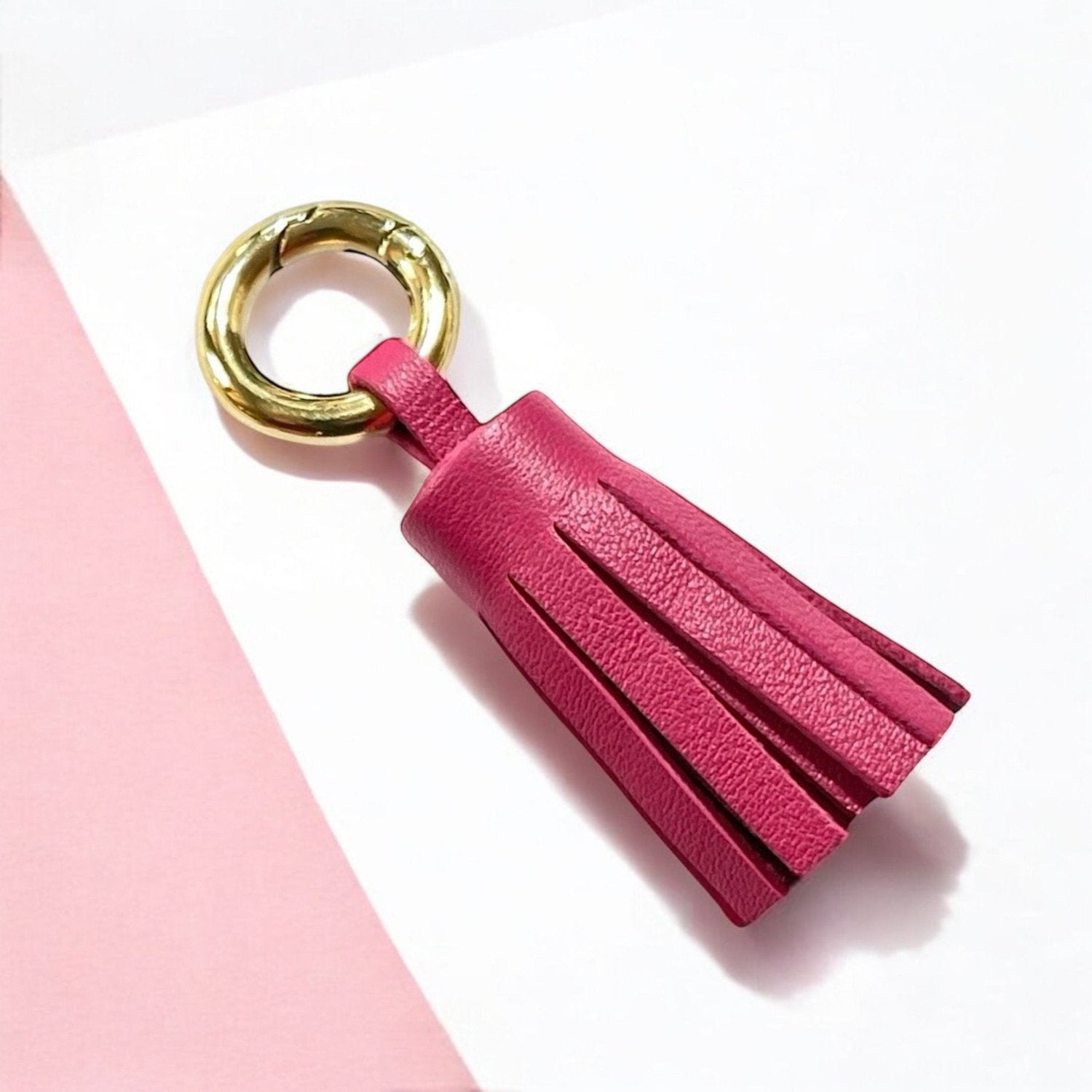 porte-clé doré en cuir fushia , en forme de pompon, sur fond blanc et rose pastel