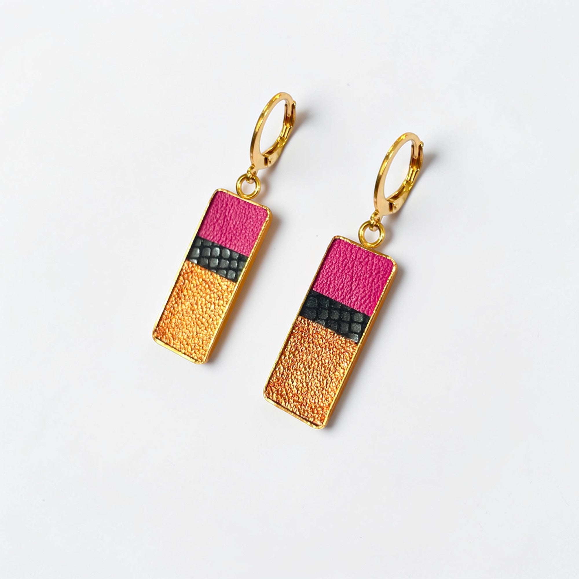 Petites boucles d'oreilles dorées pendantes rectangulaires verticales tricolores en cuirs rose fushia, noir petit grain irisé et cuivre clair, posées à plat sur fond blanc