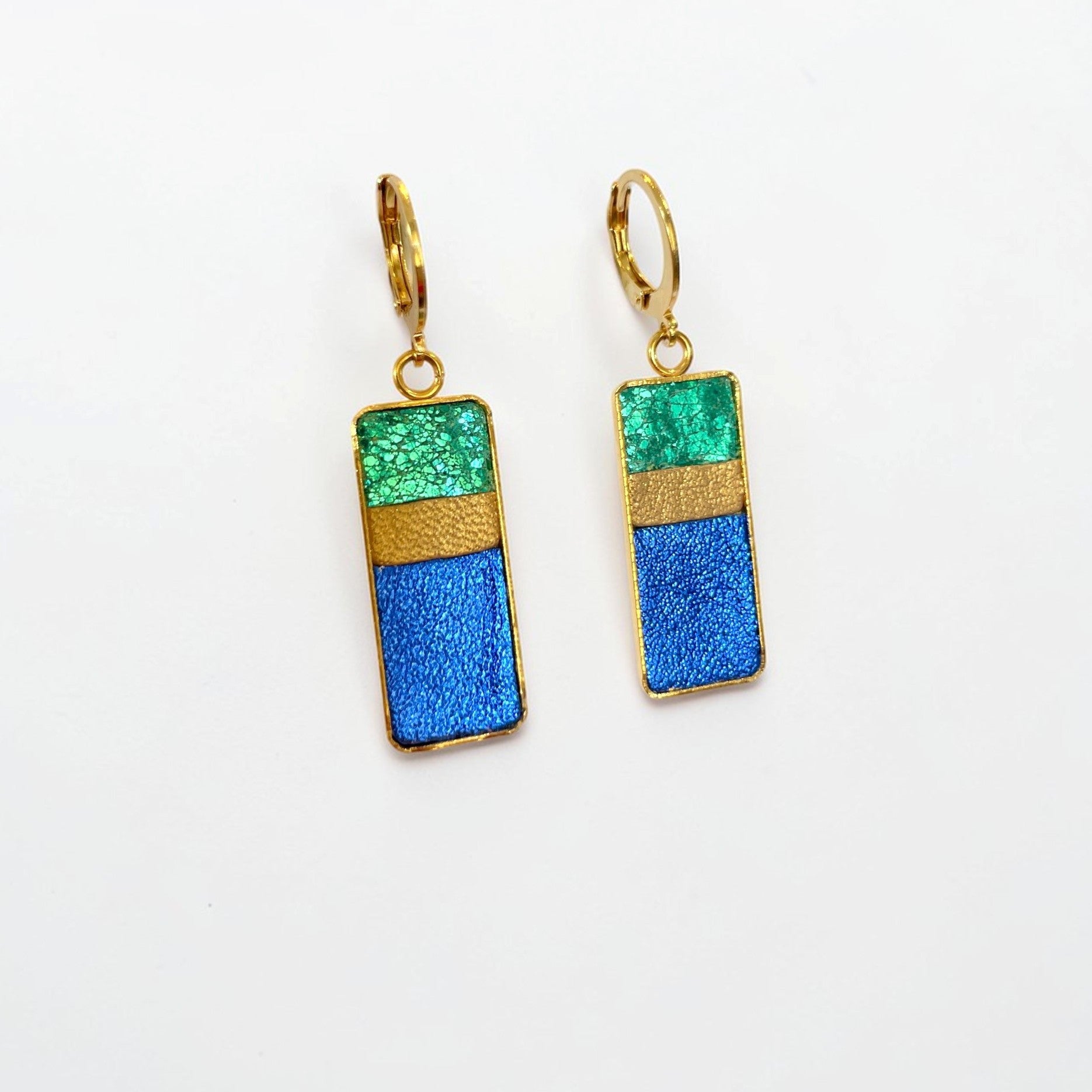 Petites boucles d'oreilles dorées pendantes rectangulaires verticales tricolores en cuirs émeraude métallisé, bronze doré et bleu cobalt métallisé, posées à plat sur fond blanc