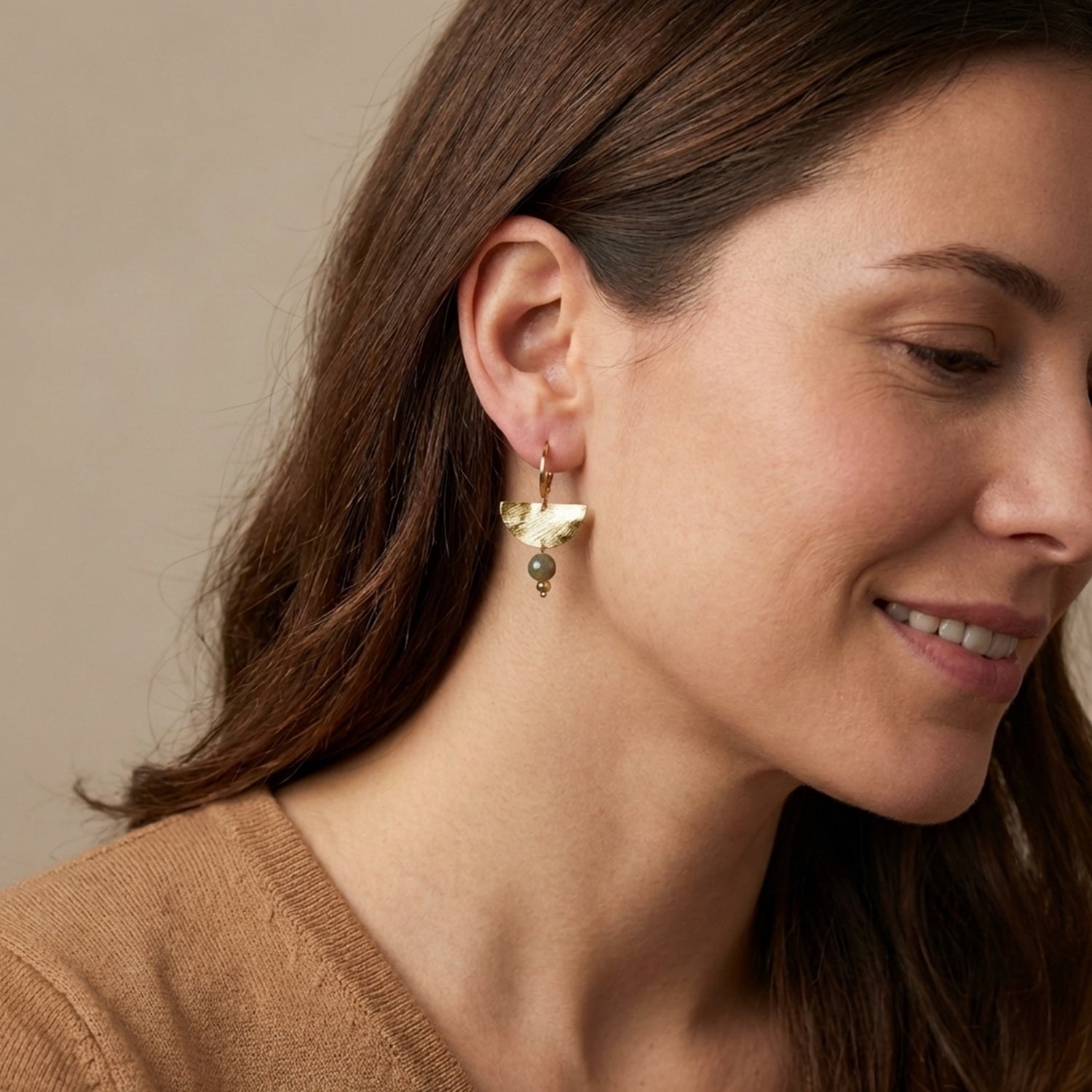 Petites boucles d'oreilles pendantes, de forme demi-lune, en métal martelé doré à l'or fin et perles de Pyrite, portées aux oreilles par une femme brune