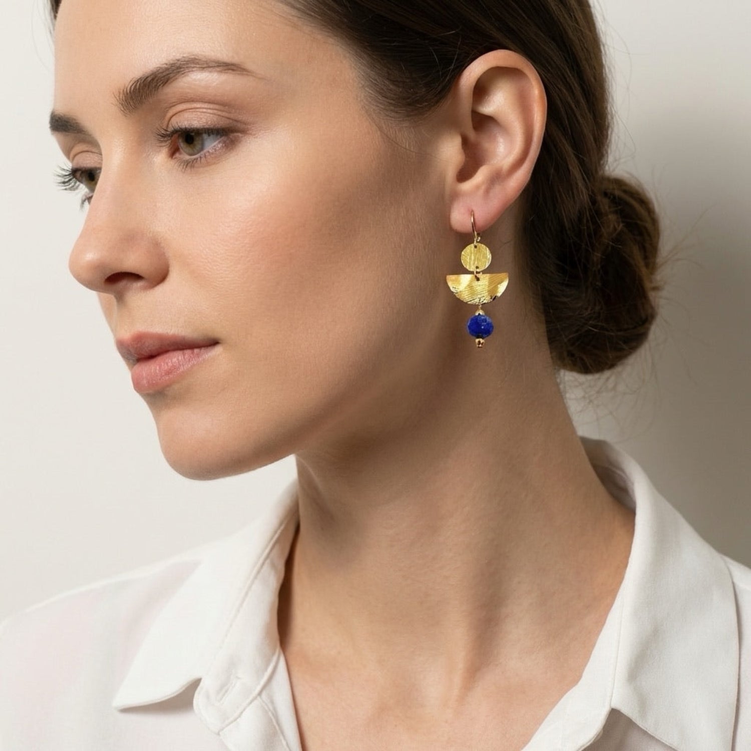 Boucles d'oreilles pendantes de forme demi-lune, en métal martelé doré à l'or fin et perles de Lapis Lazuli, portées à l'oreille