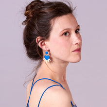 Charger l&#39;image dans la galerie, Jeune femme à chignon, vue de 3/4, portant les Boucles d&#39;oreilles dorées Vénus en forme de cœurs style ex-voto en cuir bleu roi recyclé
