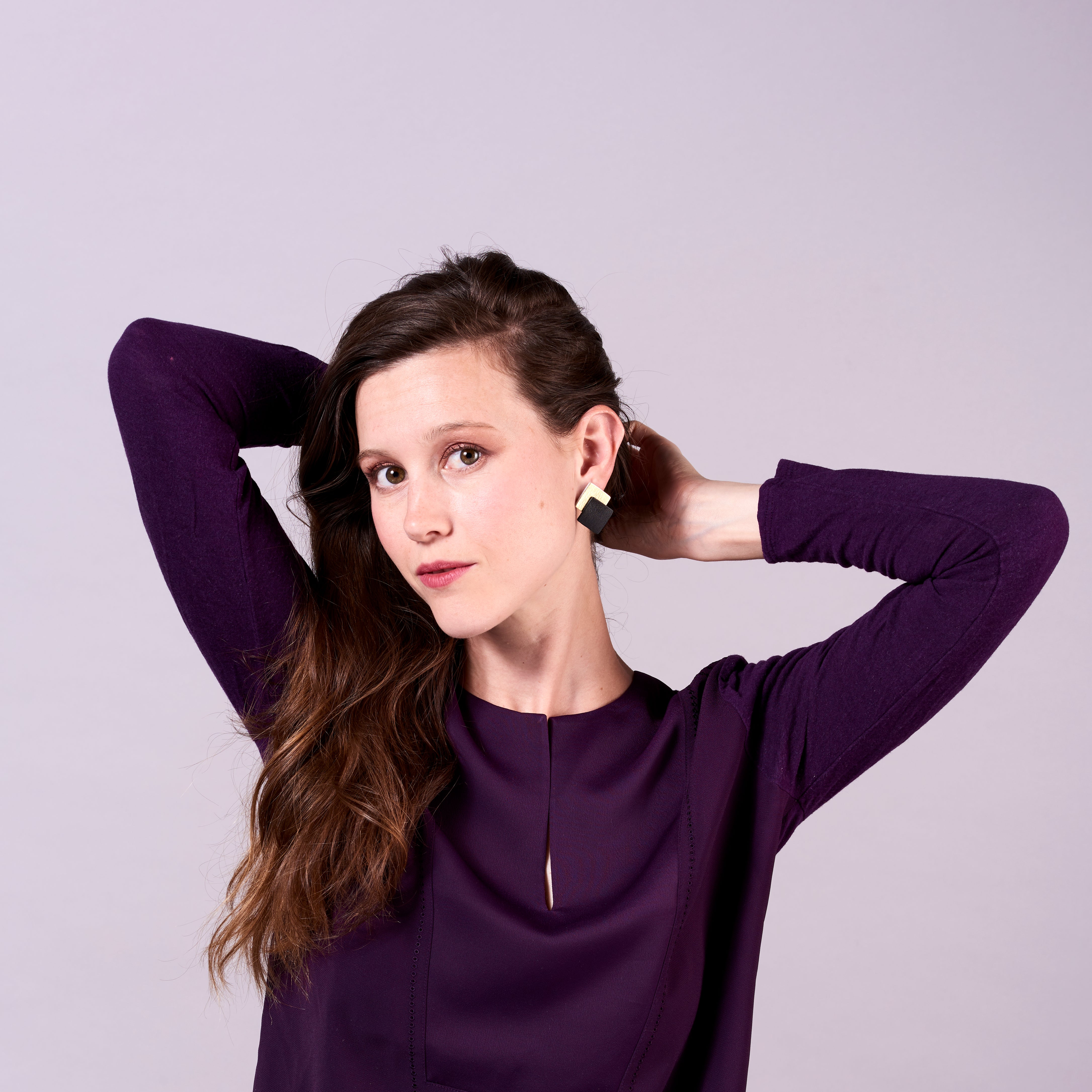 Jeune femme vue de loin portant les boucles d'oreilles puces Adalis, duo de losanges en cuir recyclé noir satiné et doré