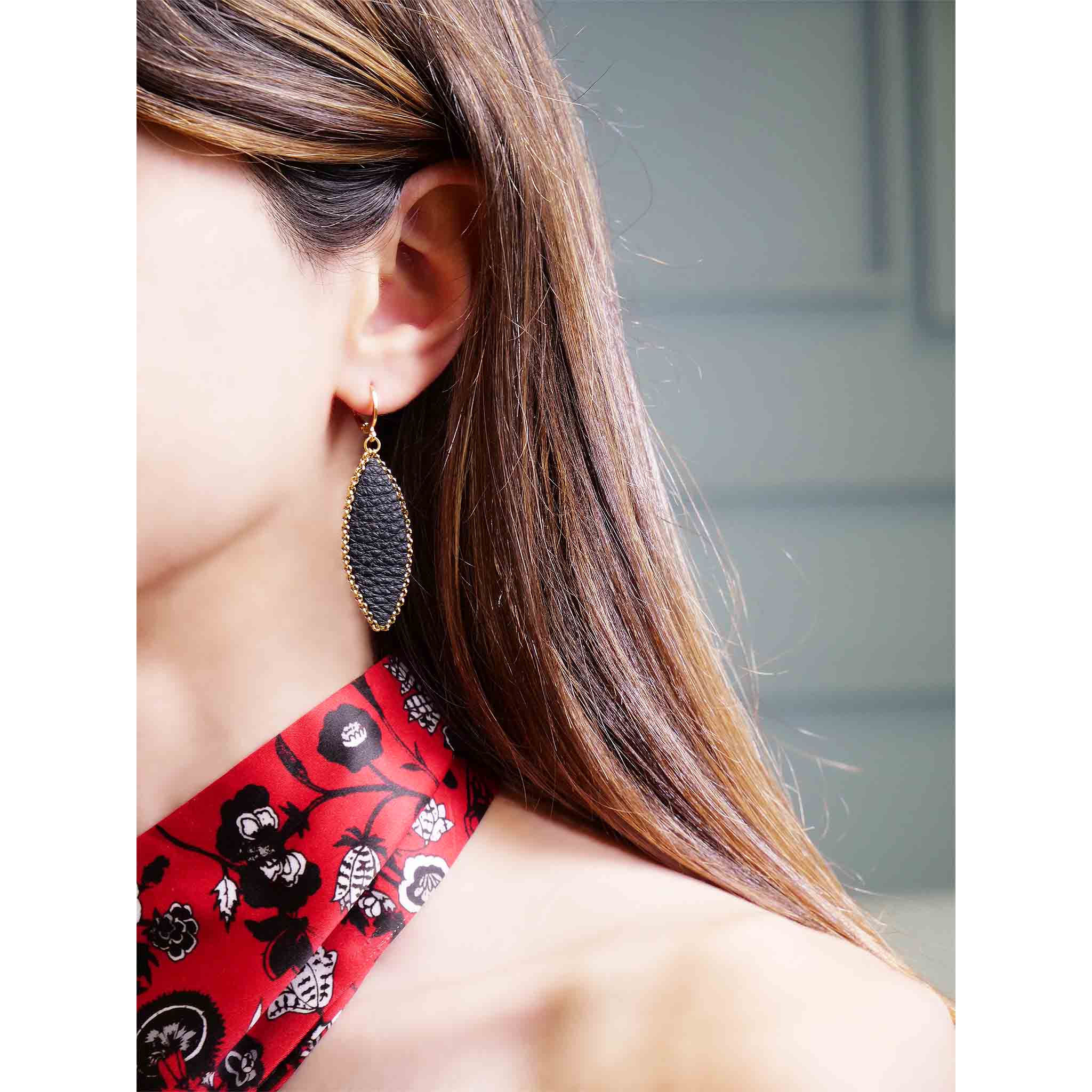 Boucle d'oreille pendante Nune modèle Auris en forme d'épi en cuir noir grainé cerclé de chaîne dorée, portée à l'oreille