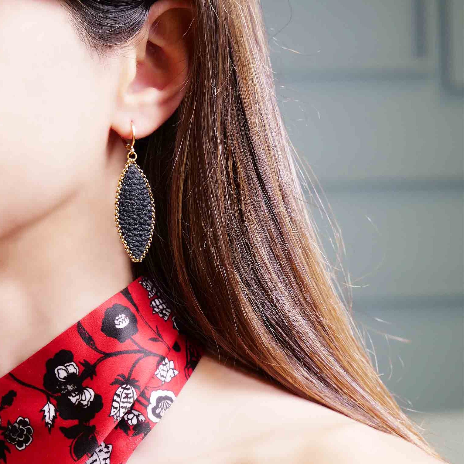 Boucle d'oreille pendante Nune modèle Auris en forme d'épi en cuir noir grainé cerclé de chaîne dorée, portée à l'oreille