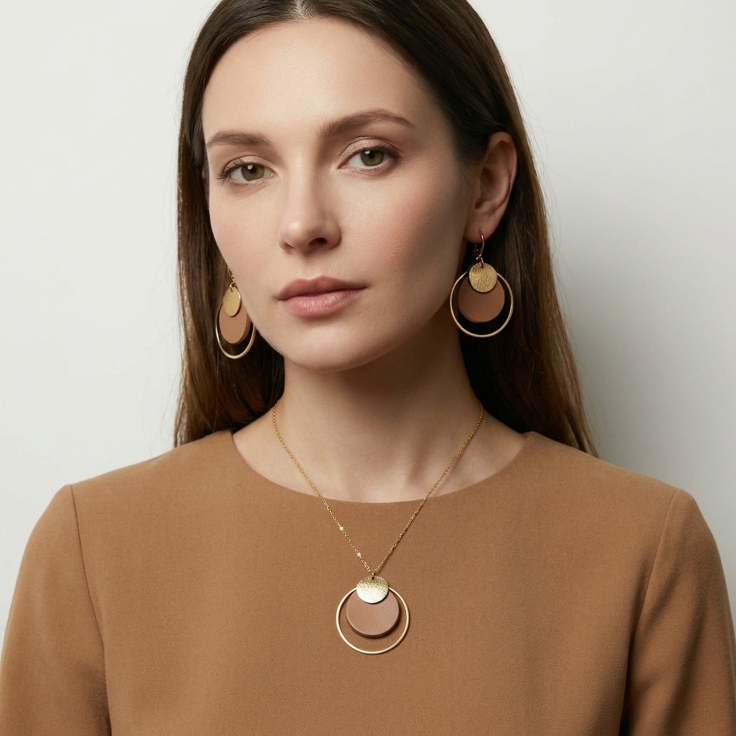 Femme brune portant la parure Danaé, collier et boucles d'oreilles dorées, en cuir brut recyclé et cuir doré, avec pendentifs de forme ronde.