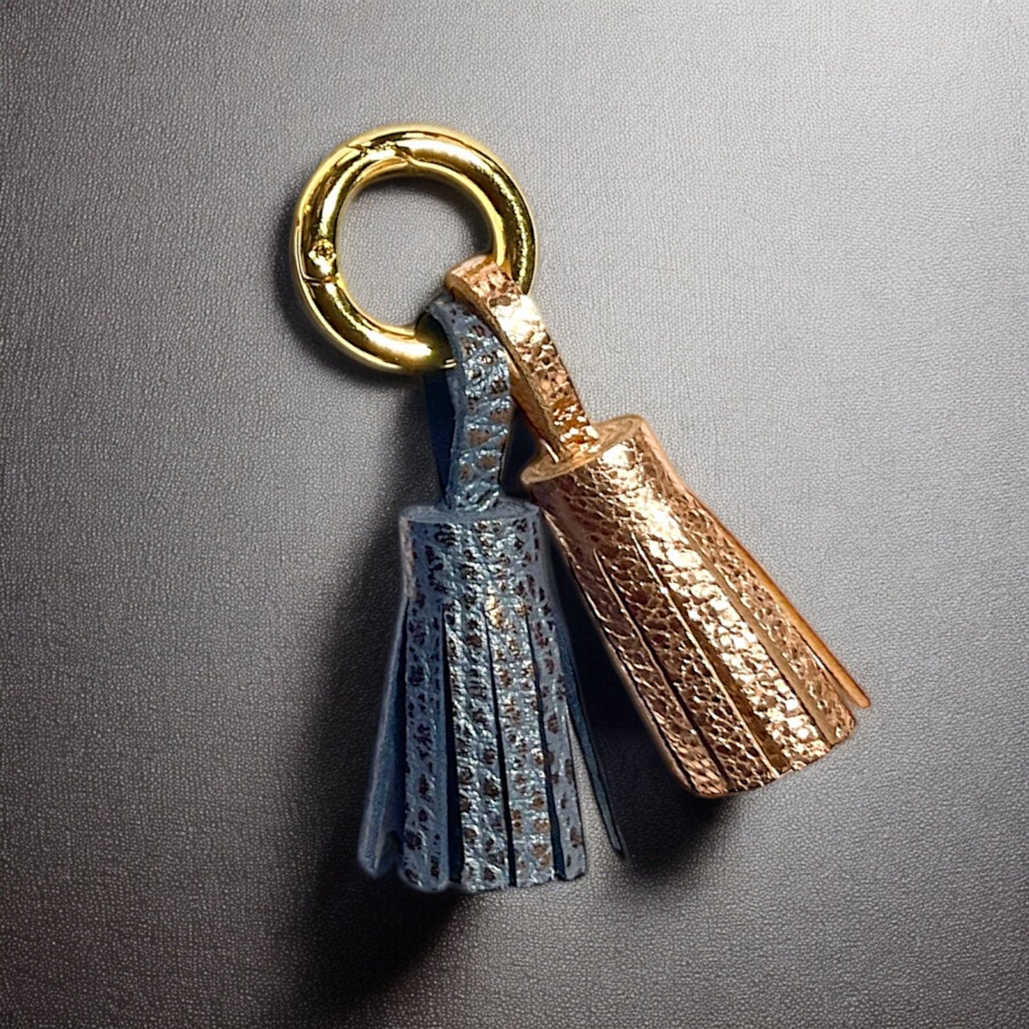 Bijou de sac doré avec 2 pompons en cuirs gris mordoré grainé et or rosé froissé, sur fond noir