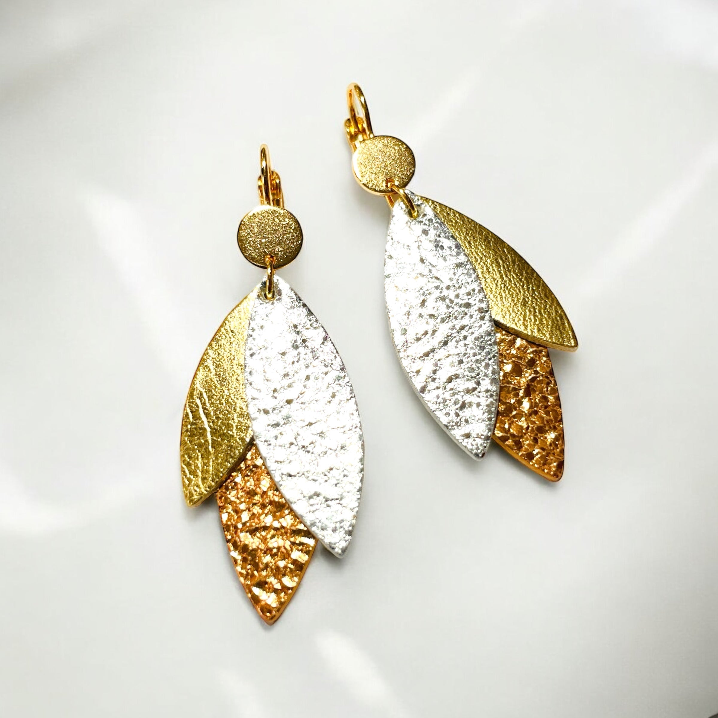 Boucles d'oreilles modÚle Ombline de la marque Nune, avec dormeuses dorées et pétales de cuirs trois Ors sur fond blanc