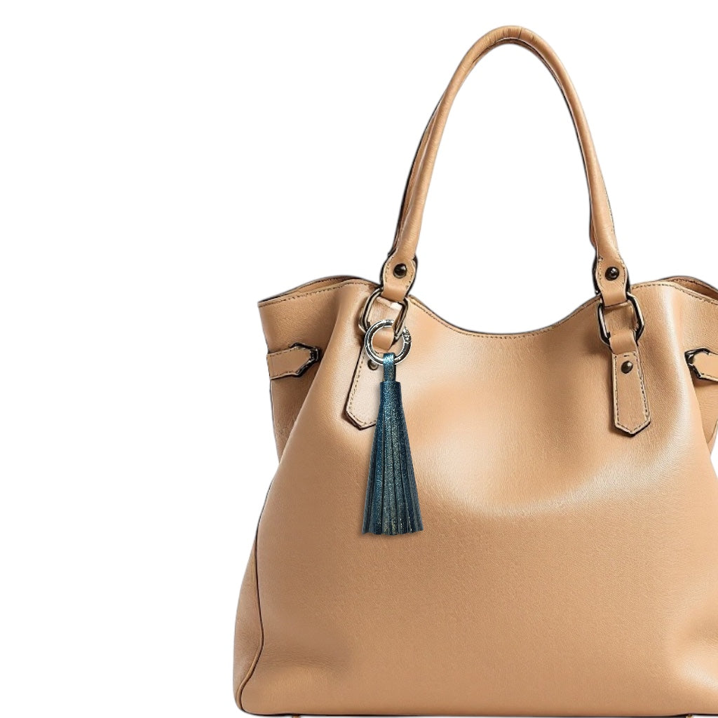 Bijou de sac argenté portant un grand pompon en cuir bleu nuit métallisé, sur un sac en cuir beige