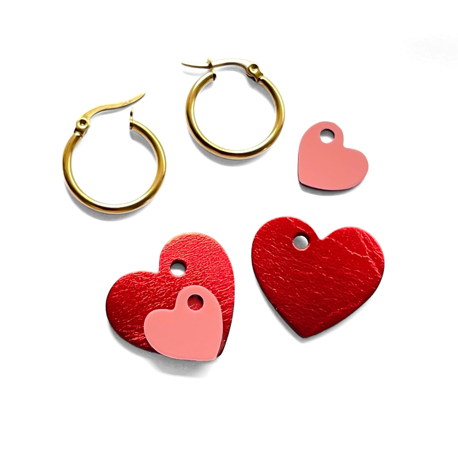 Boucles créoles dorées avec pendentifs en forme de cœurs rouge métallisé et rose vernis, posées en kit sur fond blanc