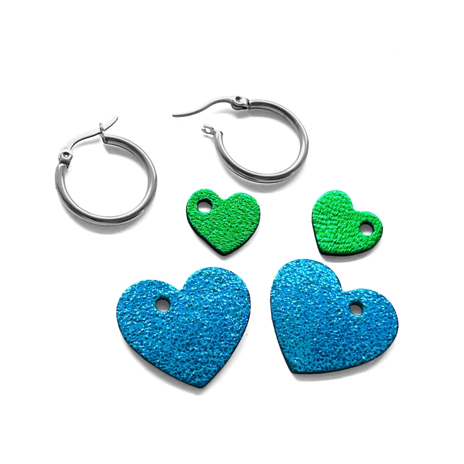 Boucles créoles argentées avec pendentifs en forme de cœurs bleu roi métallisé et vert métallisé, posées en kit sur fond blanc
