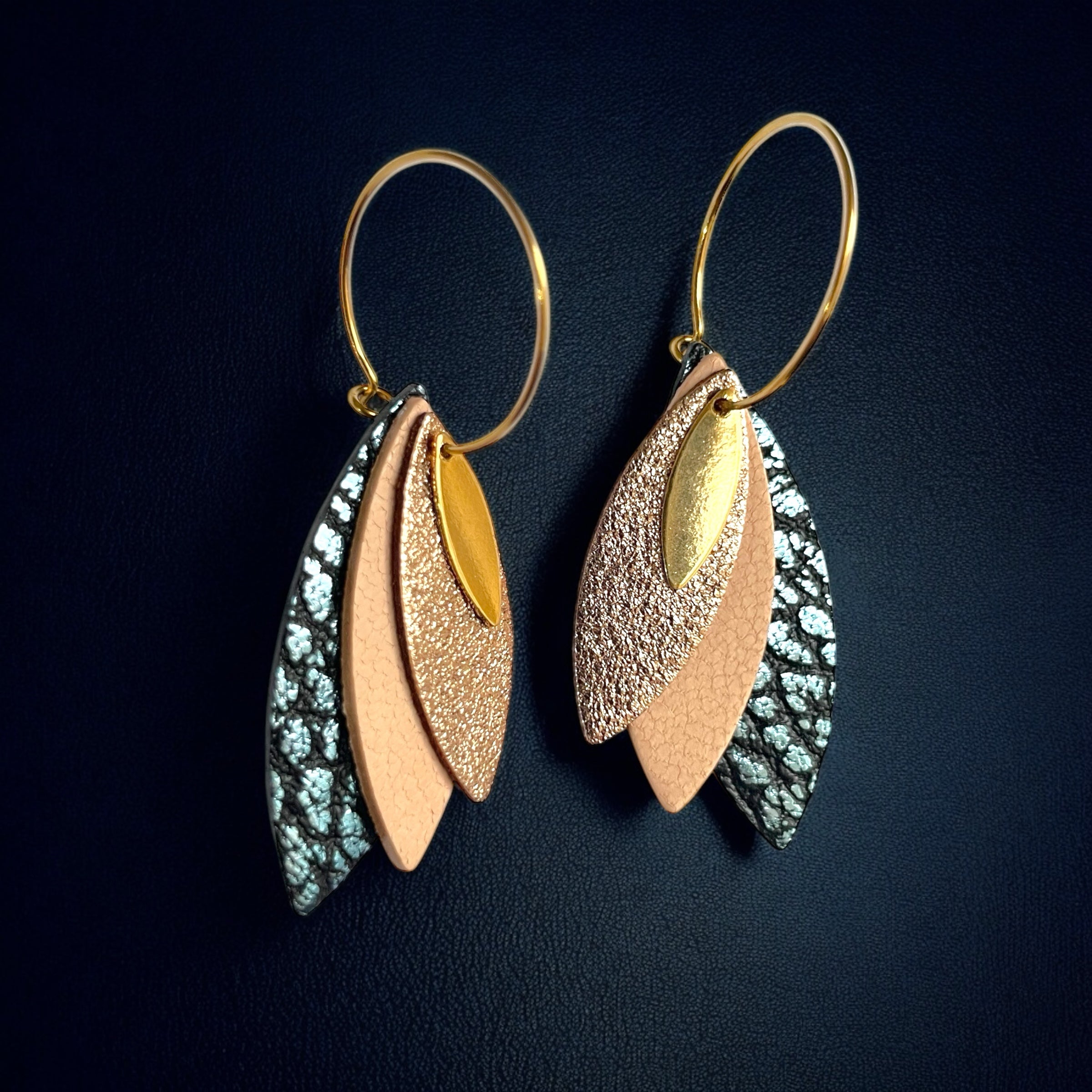 Boucles d'oreilles créoles dorées Nune modèle Piume en cuirs cannelle dorée, rose pâle et bleu glacier métallisé grainé, sur fond bleu nuit
