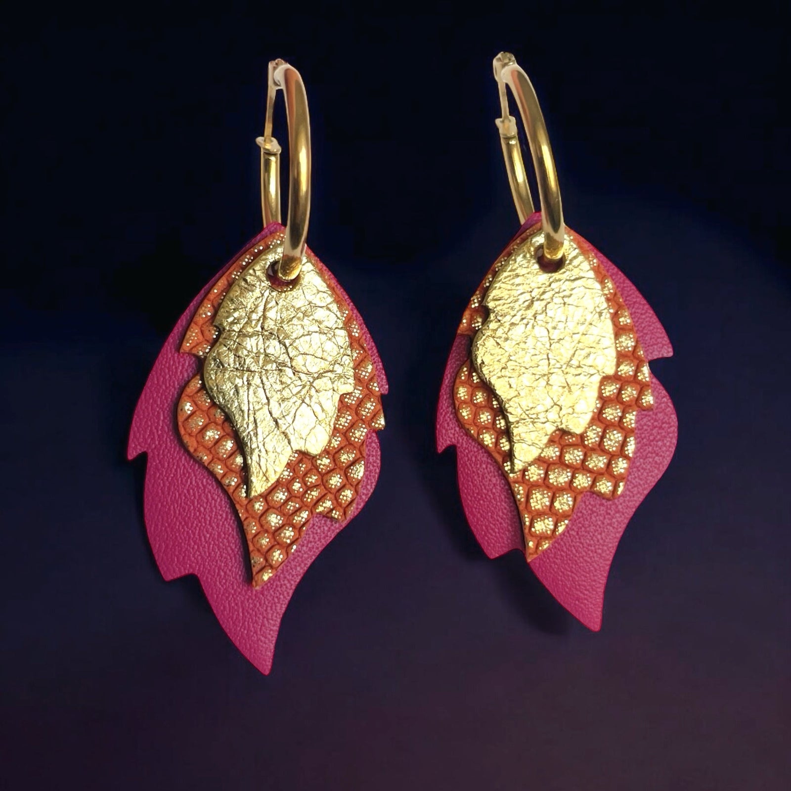Créoles dorées avec 3 pendentifs modulables en forme de flammes en cuirs doré brillant, orangé or façon serpent et fushia, vues de face sur fond violet foncé