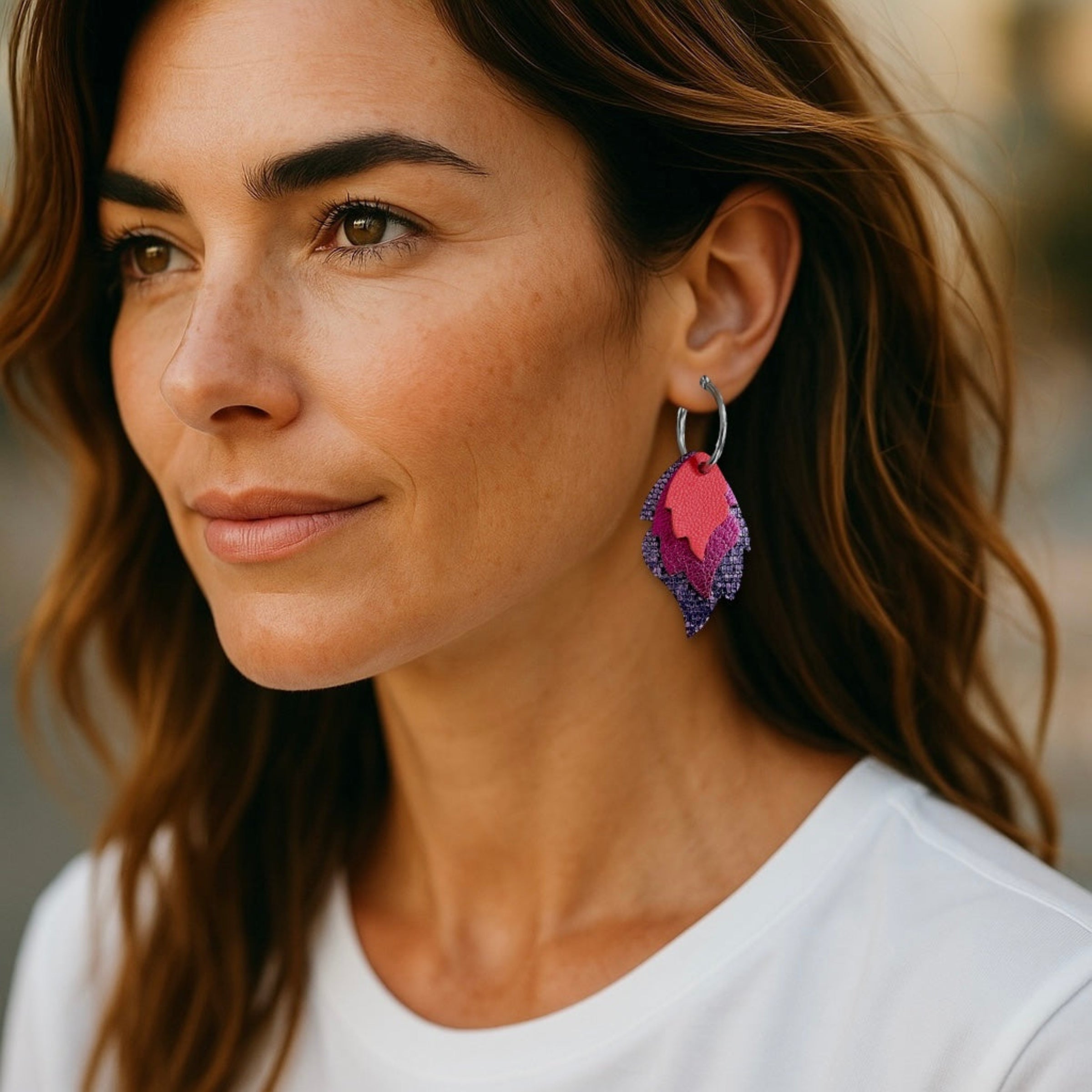 Créoles dorées avec 3 pendentifs modulables en forme de flammes en cuirs saumon, fushia métallisé et violet brillant façon serpent, portées à l'oreille par une femme brune