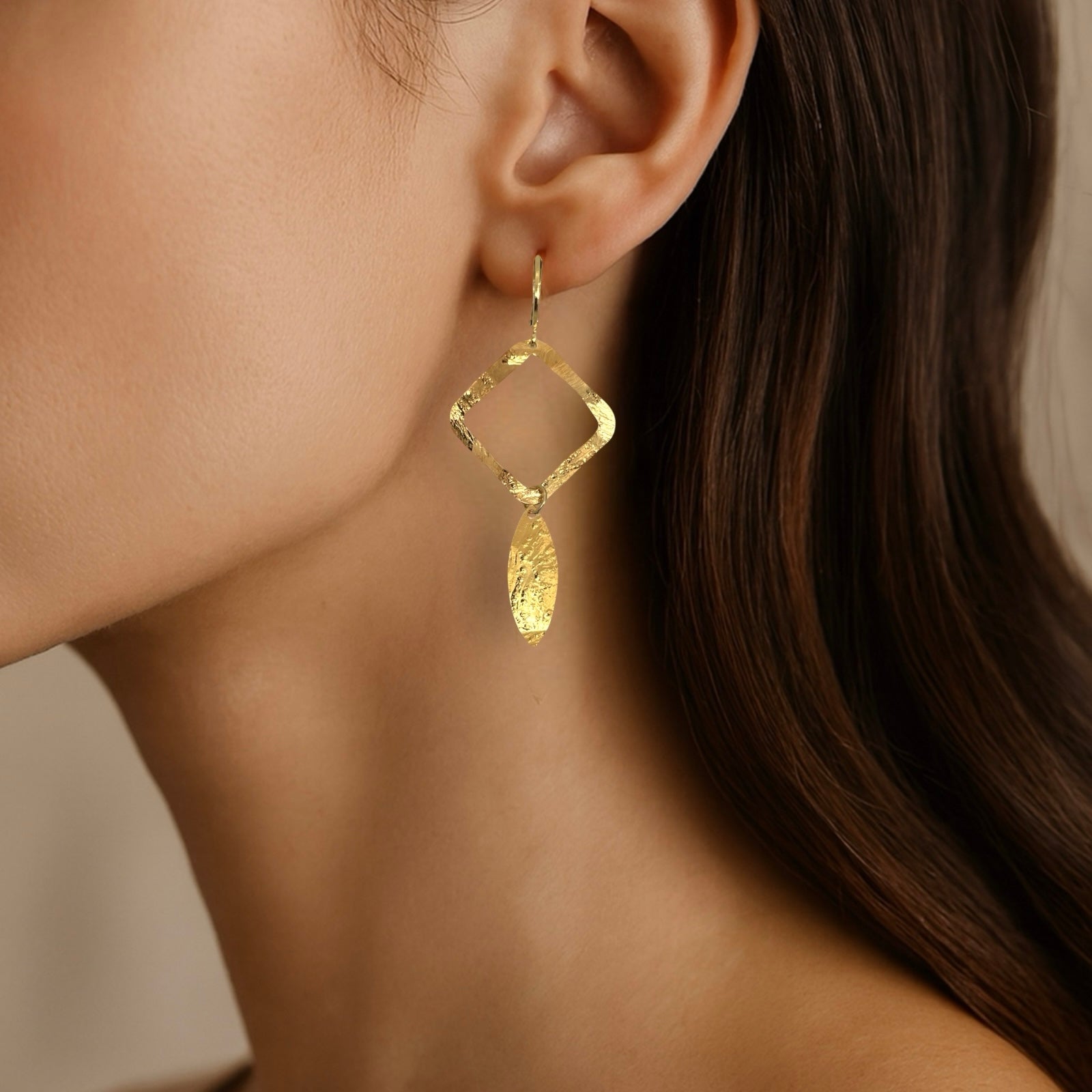 Boucles d'oreilles dorées avec pendentif en forme de losanges et pointes, portées aux oreilles