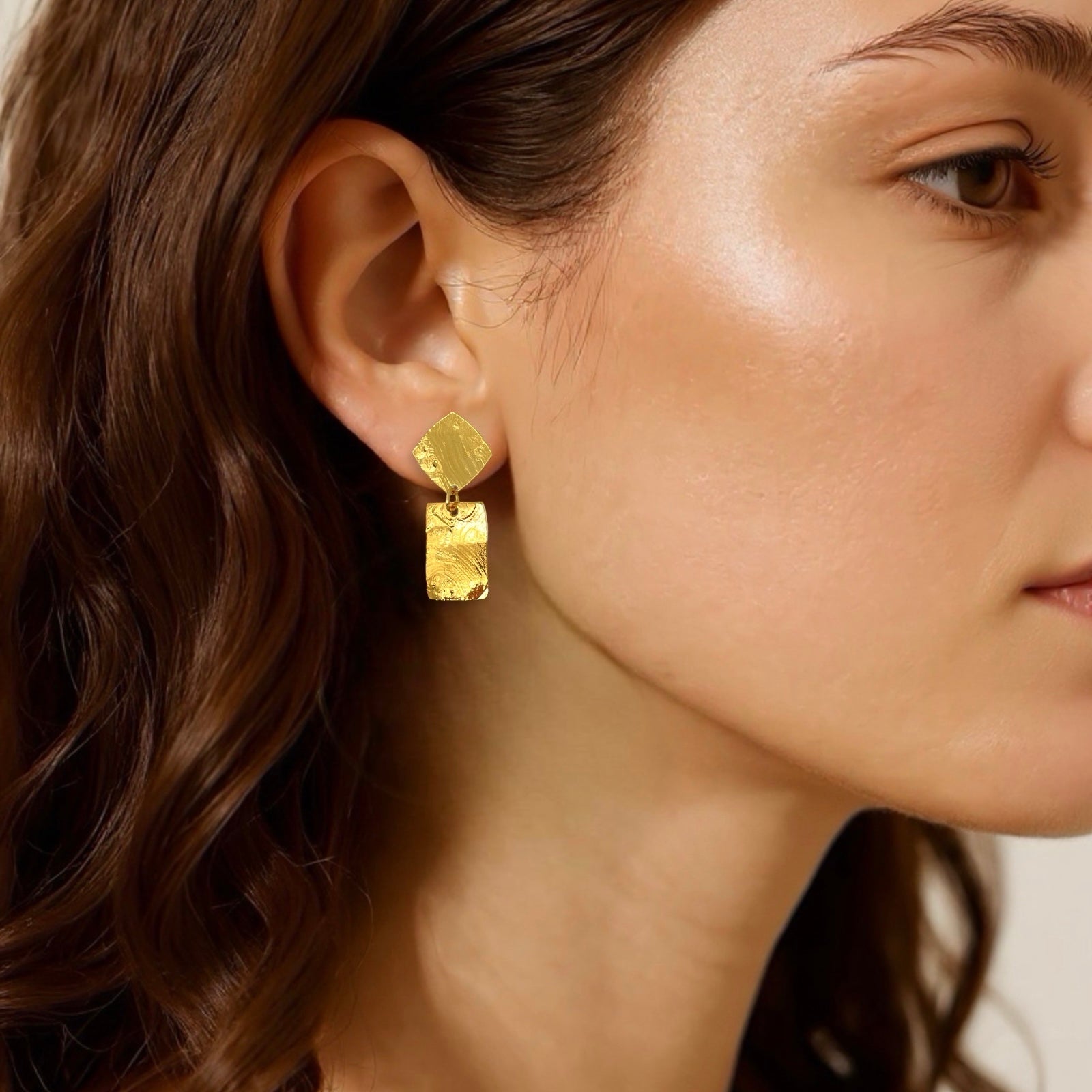 Petites puces d'oreilles losanges avec pendant rectangulaire en métal martelé doré à l'or fin, portées aux oreilles