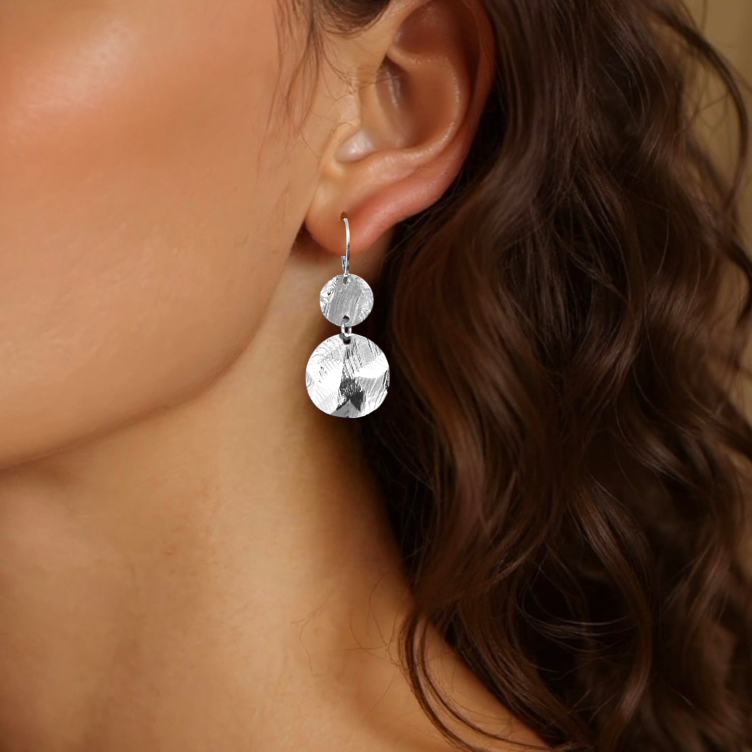 Petites boucles d'oreilles argentées pendantes avec 2 petits sequins ronds en métal martelé, portées aux oreilles
