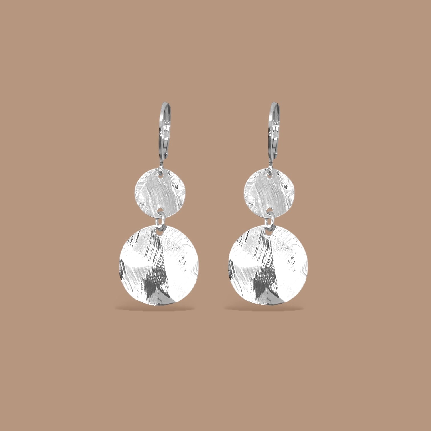 Petites boucles d'oreilles argentées pendantes avec 2 petits sequins ronds en métal martelé, sur fond beige