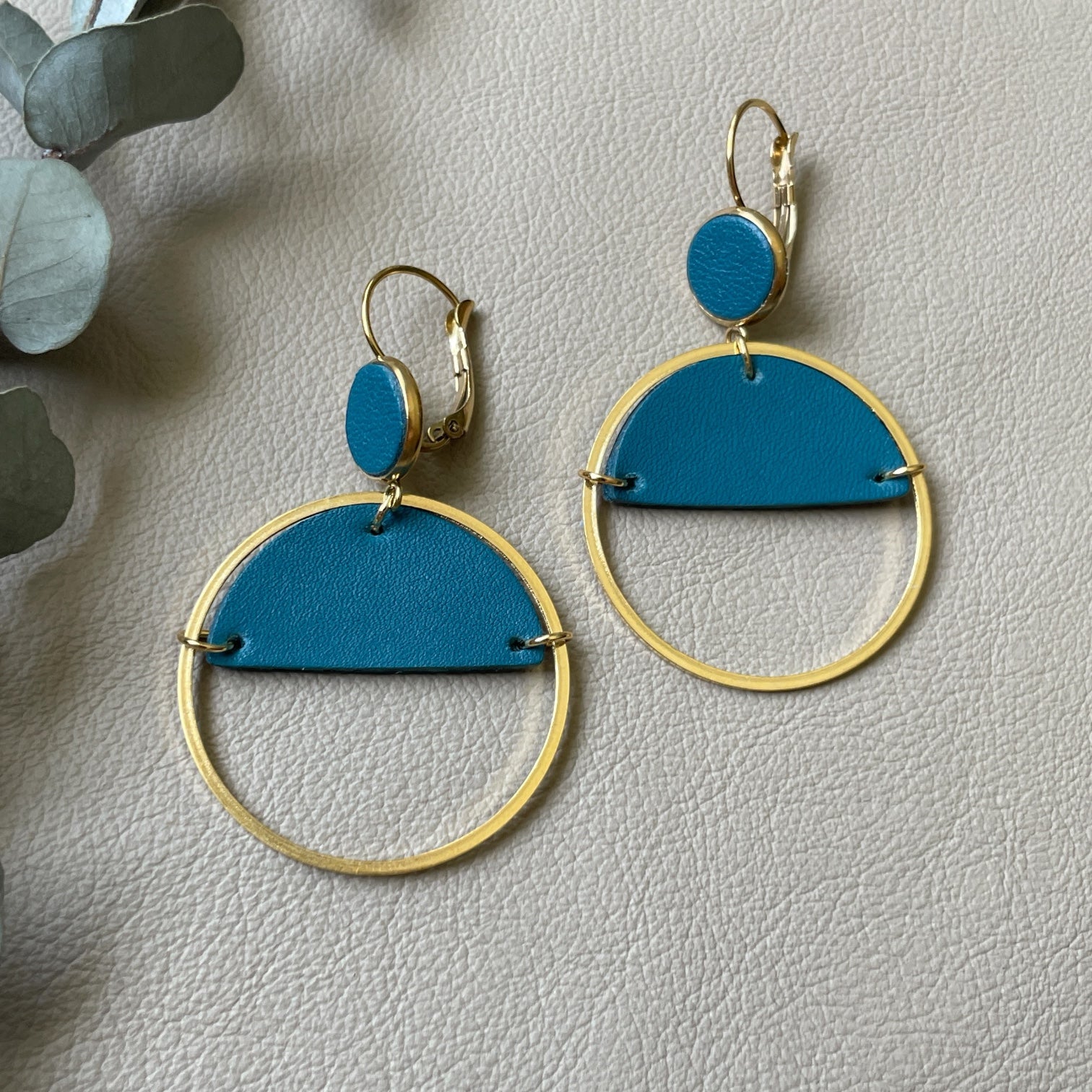 Paire de boucles d'oreilles créoles dorées Nune modèle Lua avec cuir vert canard, sur fond cuir beige doré