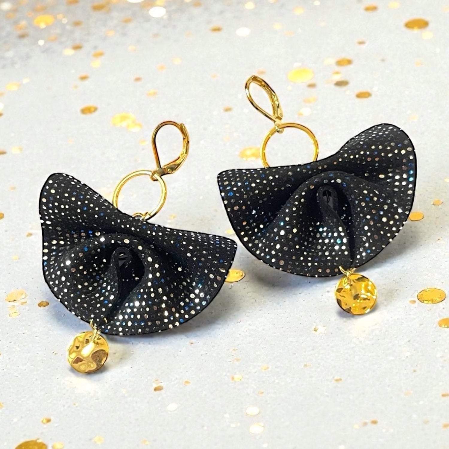 Grandes boucles d'oreilles dorées en éventails de cuir plissé noir à pois argentés et bleus, sur fond blanc avec des paillettes dorées