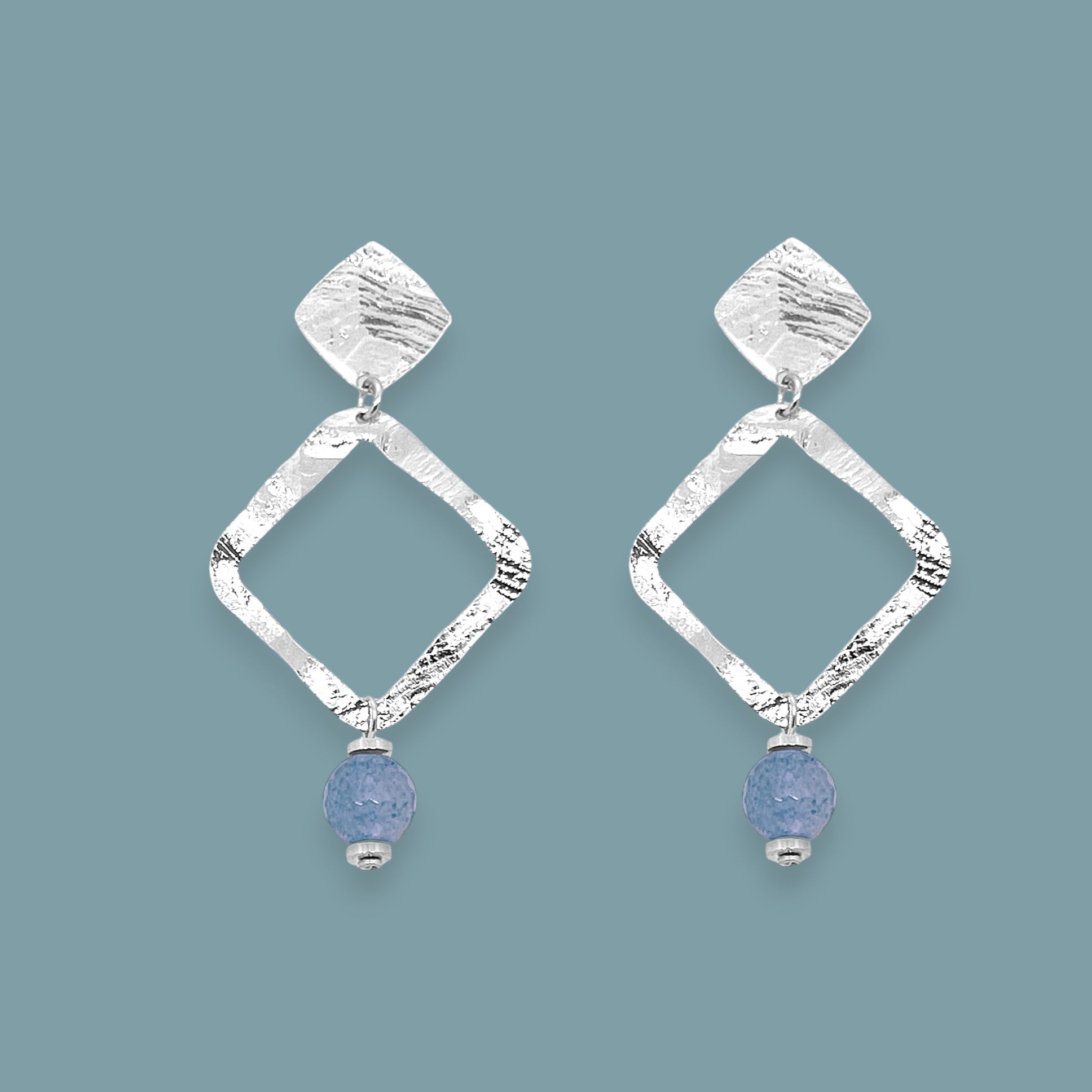 Boucles d'oreilles losanges montées sur puces en métal martelé argenté et perles d'aventurine bleu ciel, sur fond bleu gris